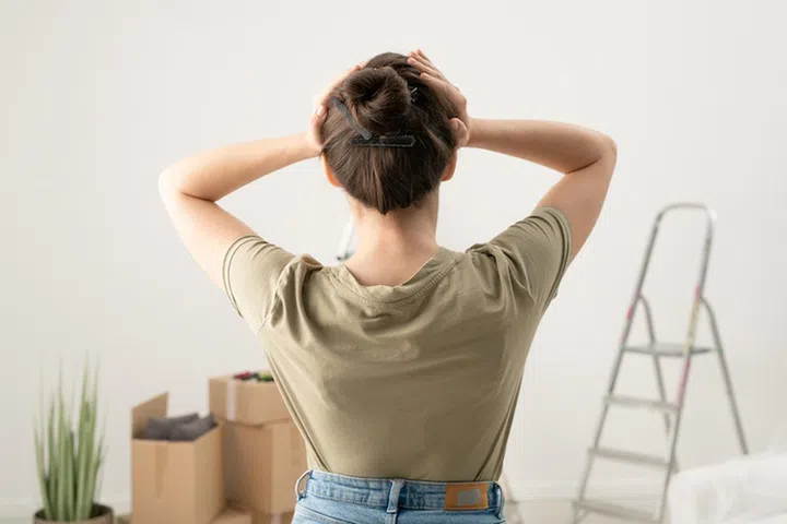 Rear view of brunette woman holding head in hands while feeling headache from fixing things in apartment
