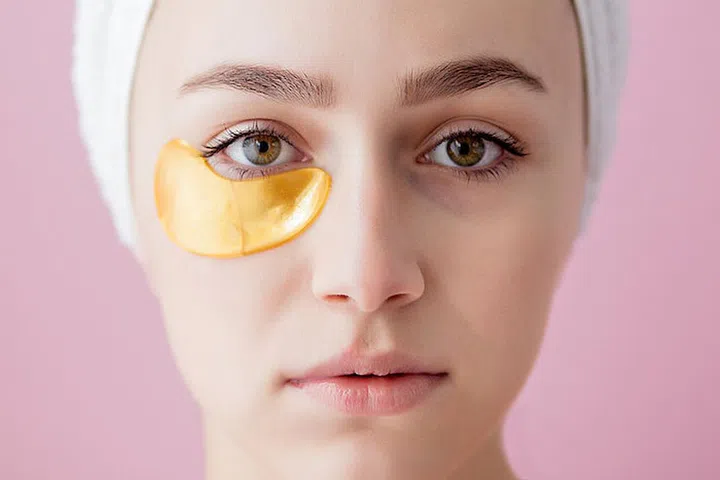 Portrait of Beauty Woman with Eye Patches on pink background. Woman Beauty Face with Mask under Eyes. Beautiful Female with natural Makeup and Gold Cosmetics Collagen Patches on Fresh Facial Skin.