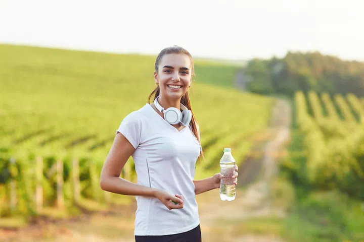 Brunette girl runner with a bottle of water is in training against the background of vineyards. Active lifestyle.