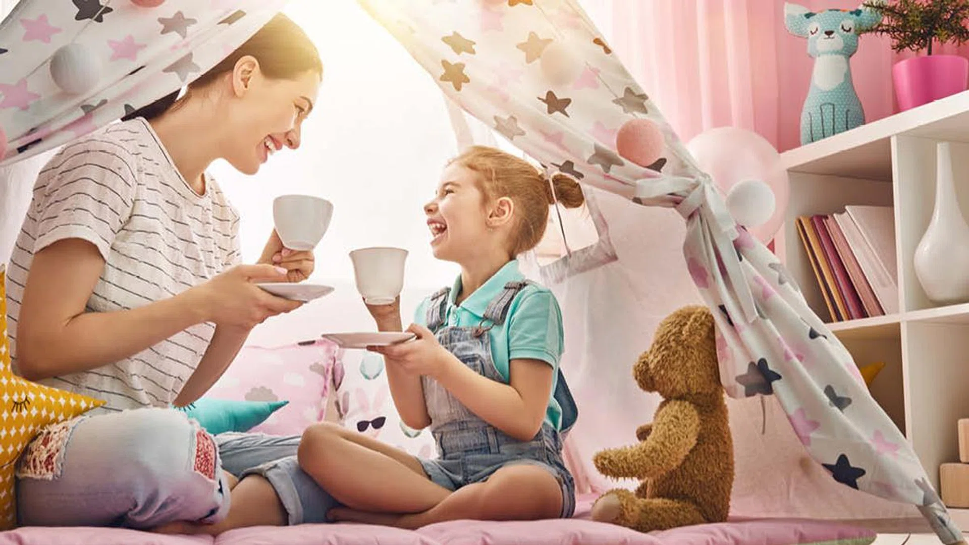 A mother and daughter having tea in a teepee tent.