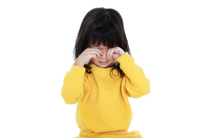 Chinese child waking up, girl looks sleepy in the morning, isolated on white background. A tired asian girl in pajamas rubbing eyes.