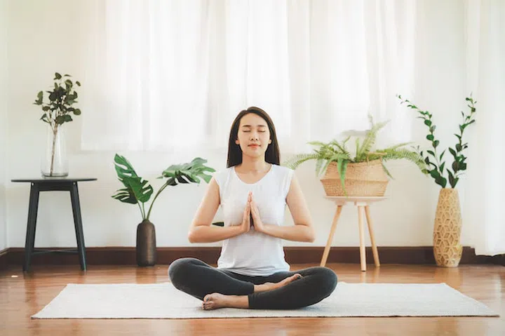 Shot of attractive healthy Asian woman doing yoga meditation at home in living room