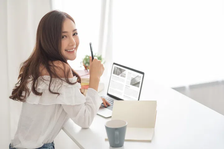 Portrait of beautiful Asian woman smiling and looking at camera during working with laptop computer. Female Blogger and freelance. Online shopping. Small Business owner. SME.