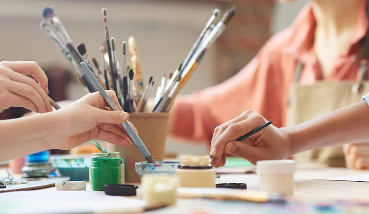 Close-up of children using paintbrush and watercolor paints to paint a pictures at the table