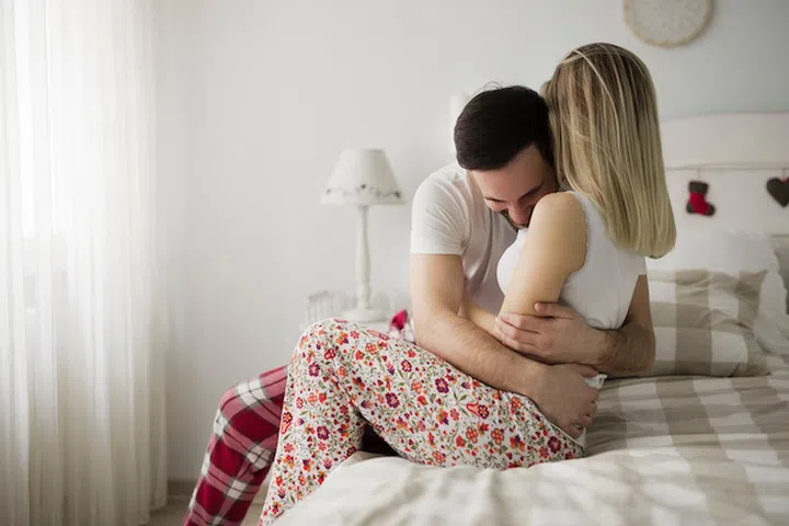 Picture of young attractive couple hugging on their bed