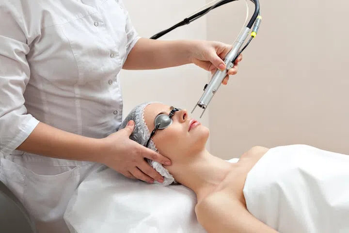 Woman lying on a table with protect glasses on eyes getting a laser skin treatment in healthy beauty spa salon