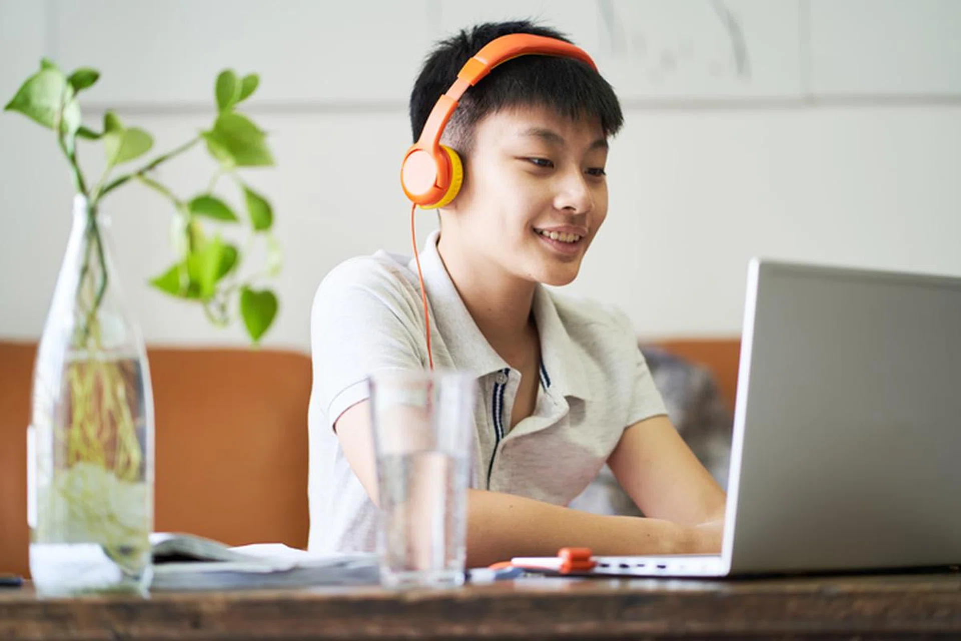 Asian teenage boy studying at home during pandemic wearing headset smiling