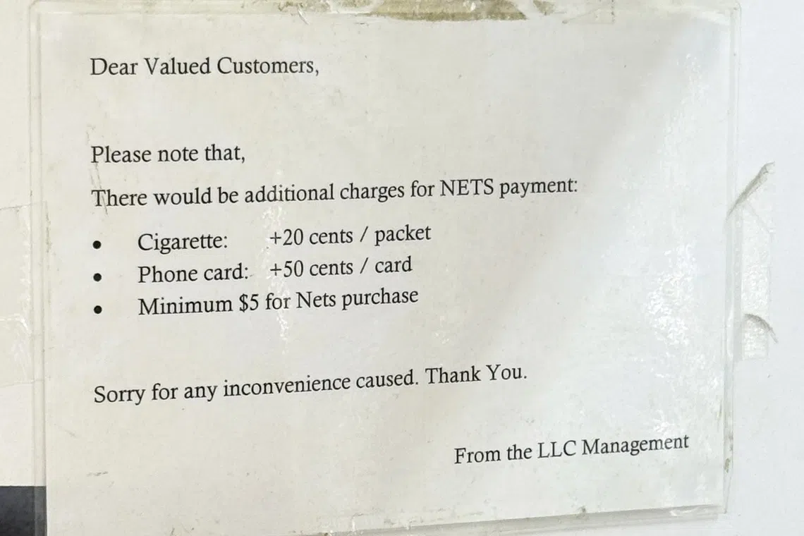 收银处的告示注明，顾客若通过NETS付费购买香烟与手机卡，需要多付钱。（纪允贤摄）