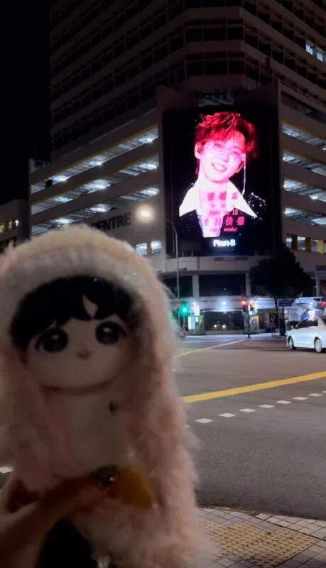 粉丝特地带着公仔与偶像广告屏合照。（粉丝提供）