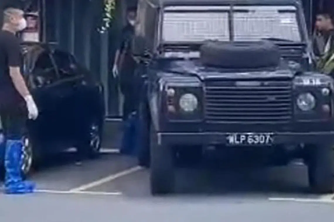 马国警员脚穿套子，把两具尸体搬上黑车。（星洲日报视频截图）