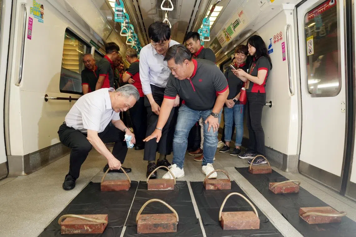 佘文民（左一）与SMRT集团总裁鄞云斌（白衣，中）到地铁车厂视察，听员工向他们讲解如何为旧列车重新铺设地垫。（谢智扬摄）