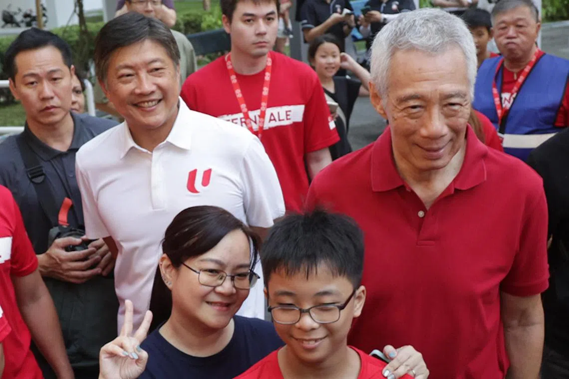 国务资政李显龙（右）与黄志明（白衣），3月16日在惹兰加由区的芬维尔社区活动上与居民合照。（蔡家增摄）