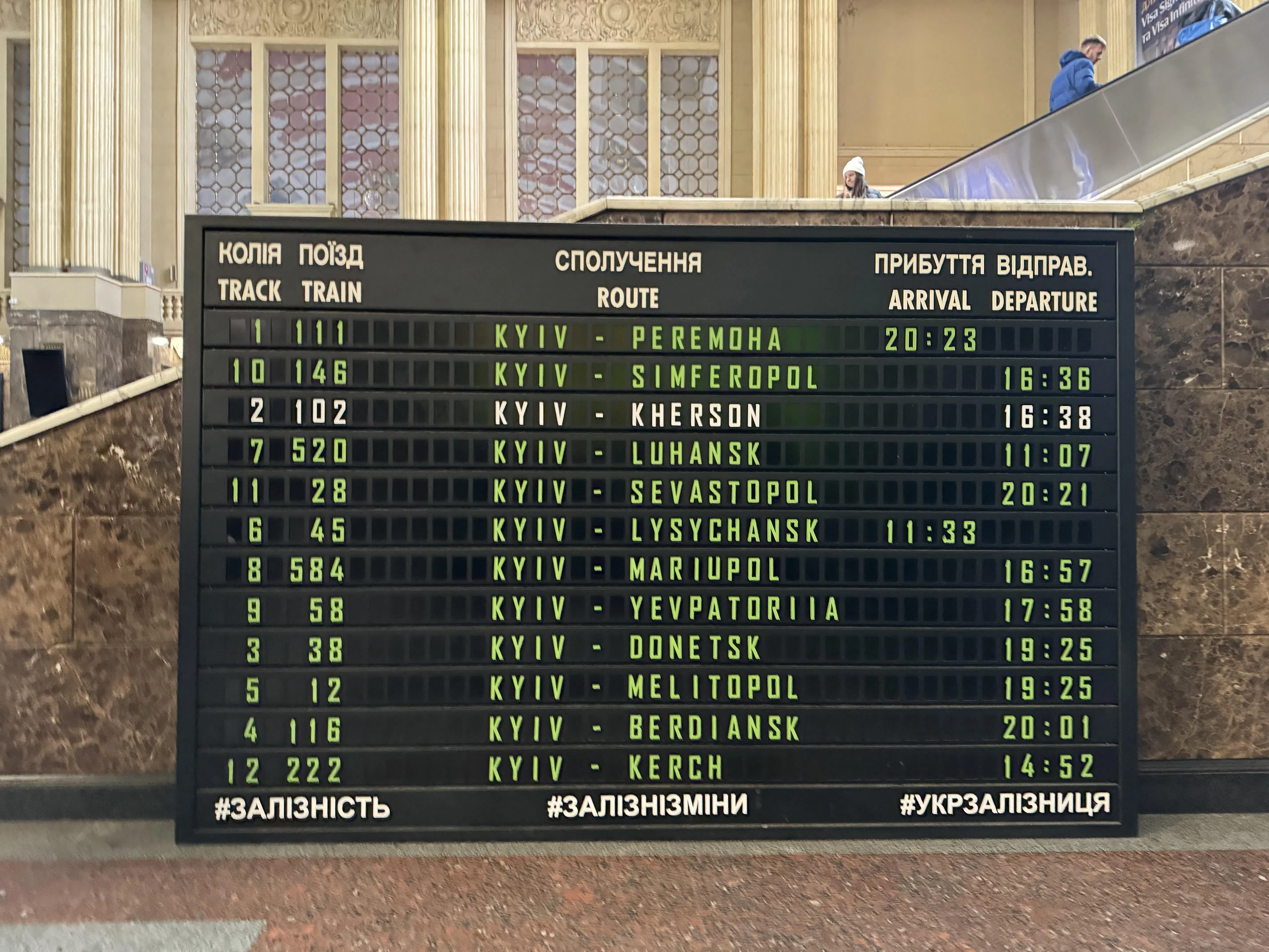 基辅火车总站大厅摆放着电子牌，第一行写着“基辅迎向胜利”，时间为2023年。其它是从基辅通往被俄军占领的乌克兰城市路线，并标出一旦被乌军收复后，第一趟从基辅出发，开向该城市的列车时间。在11条路线中，只有基辅开往赫尔松的路线变白色，代表乌军成功收复赫尔松。图摄于2023年11月25日。（沈泽玮摄）