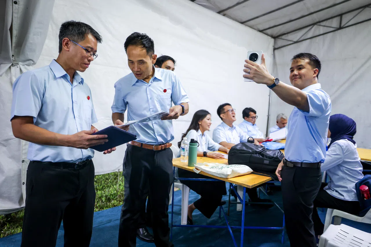 工人党4月24日在盛港安谷弯The Vales公寓旁的草场举行群众大会。活动开始迎接沸腾群众之前，候选人在后台贮备就绪，严燕松（左起）和符策涫在讨论演讲稿，而刘宇扬则拿起手机自拍，捕捉团队的幕后花絮。（叶振忠摄）