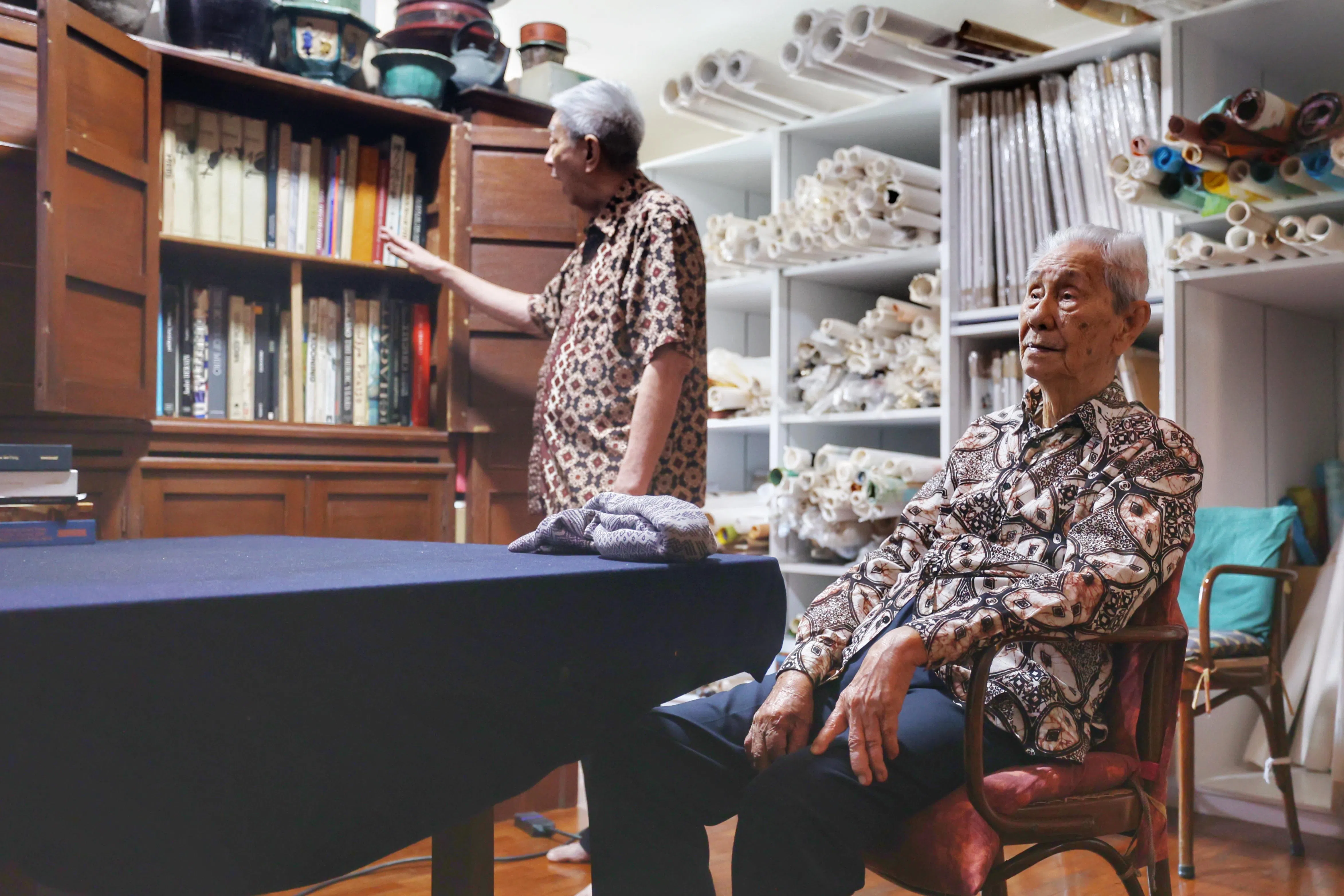 林子平长子林树国（左）打开父亲的书橱，展示收藏的名家画册。这些全是林子平的创作养分。（郑一鸣摄）