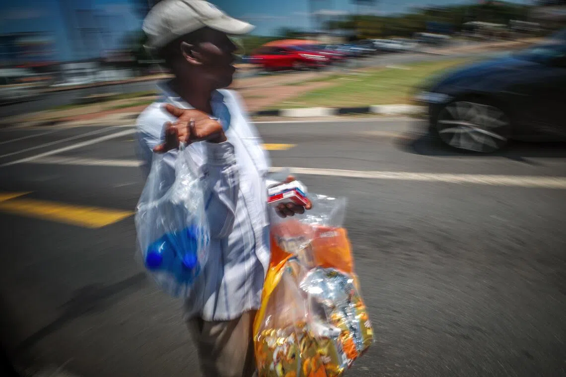 站在路边的街头小贩，手中的塑料袋装满商品，等待着路过的车辆或行人光顾。（叶振忠摄）