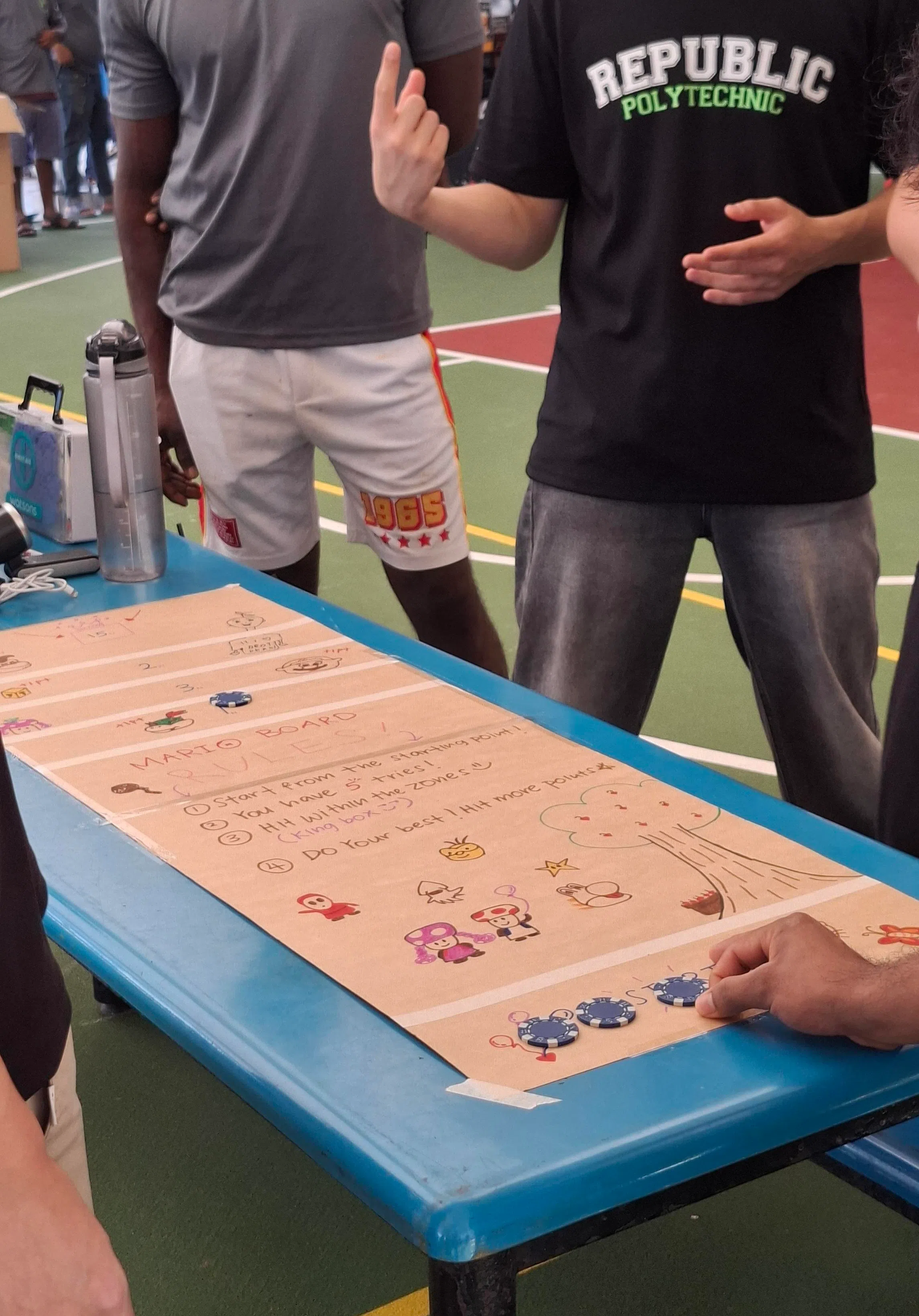 共和理工学院学生向客工讲解“硬币滑滑乐”的游戏规则。（南洋初级学院提供）