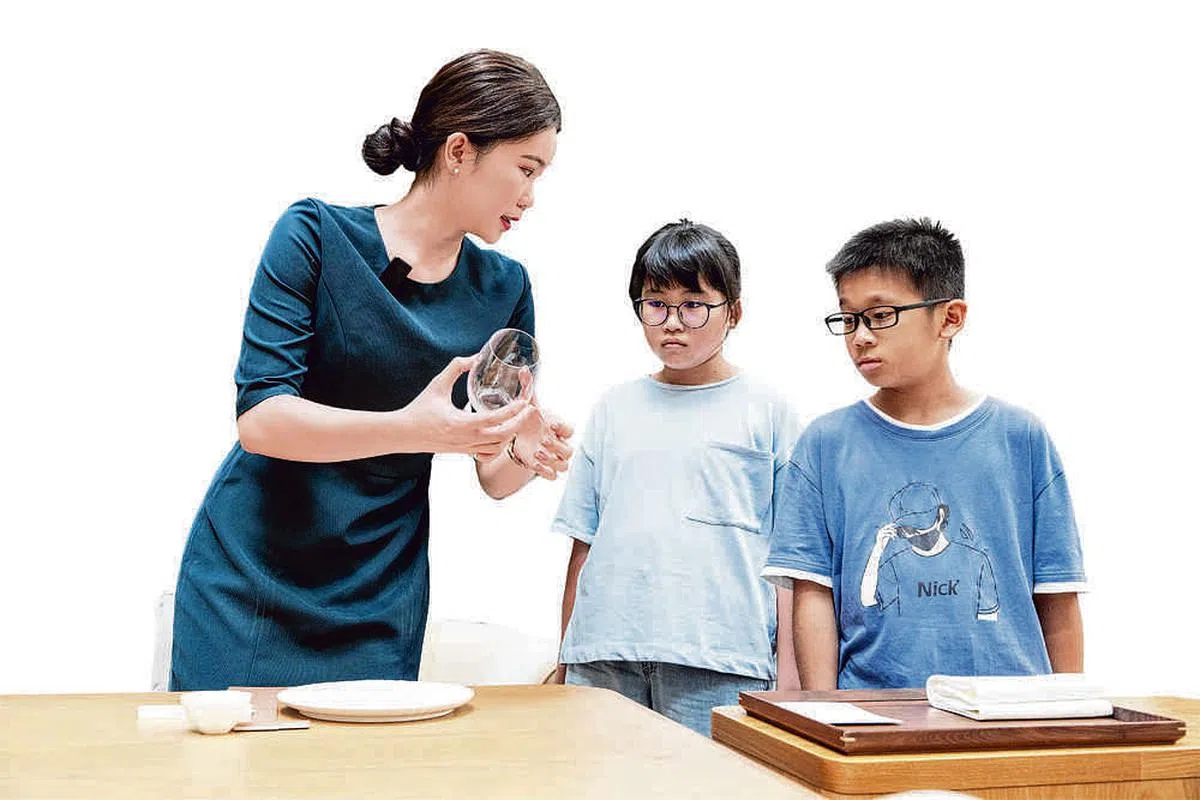摆放餐具也很讲究细节，餐厅领班余璎祺（左）教两位“小学徒”摆放餐具要注意的事项。