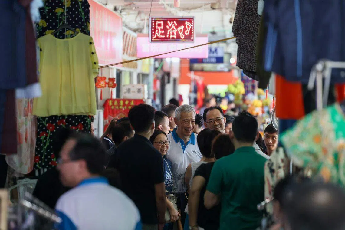 李总理（中，白衣）在邻里派发红包封套，引来许多公众争相与他合照留念，他也大方接受大家的要求。（卓祾祎摄）