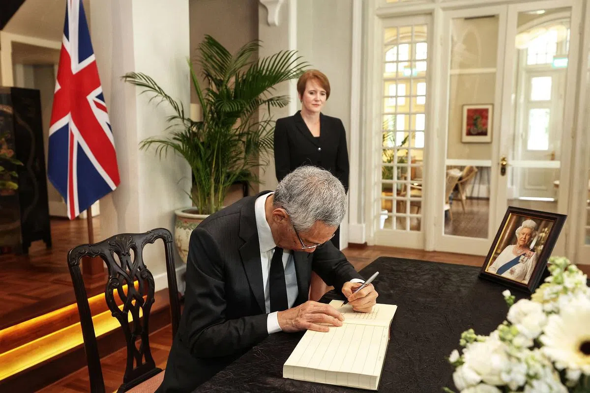 李显龙总理（前）到英国驻新加坡最高专员欧文（后）官邸悼念英女王，并在吊唁册上留言。（通讯及新闻部提供）