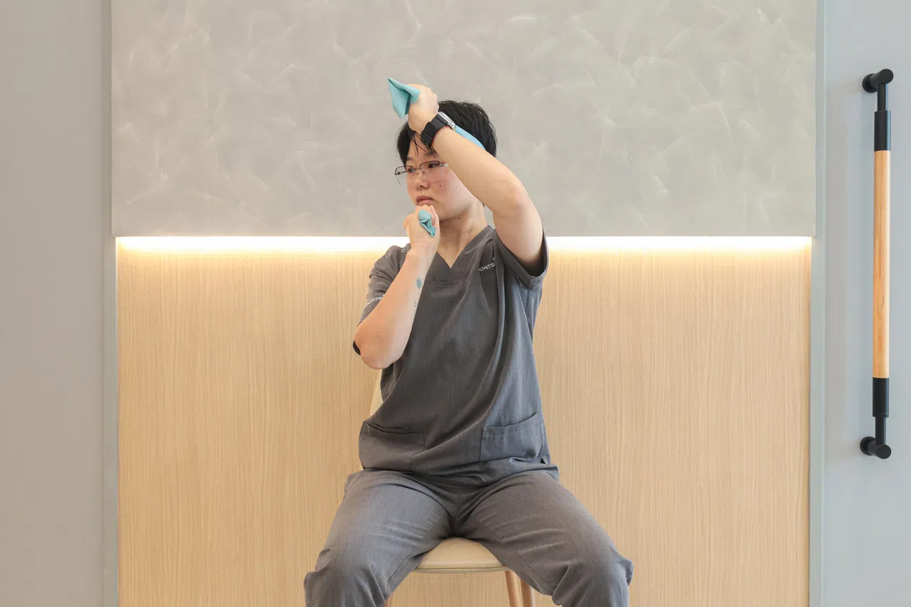 右手弹力带紧靠耳朵下方，左手弹力带紧靠耳朵上方。左手向右用力，让毛巾带动头部向右旋转至最大角度。（李冠卫摄）