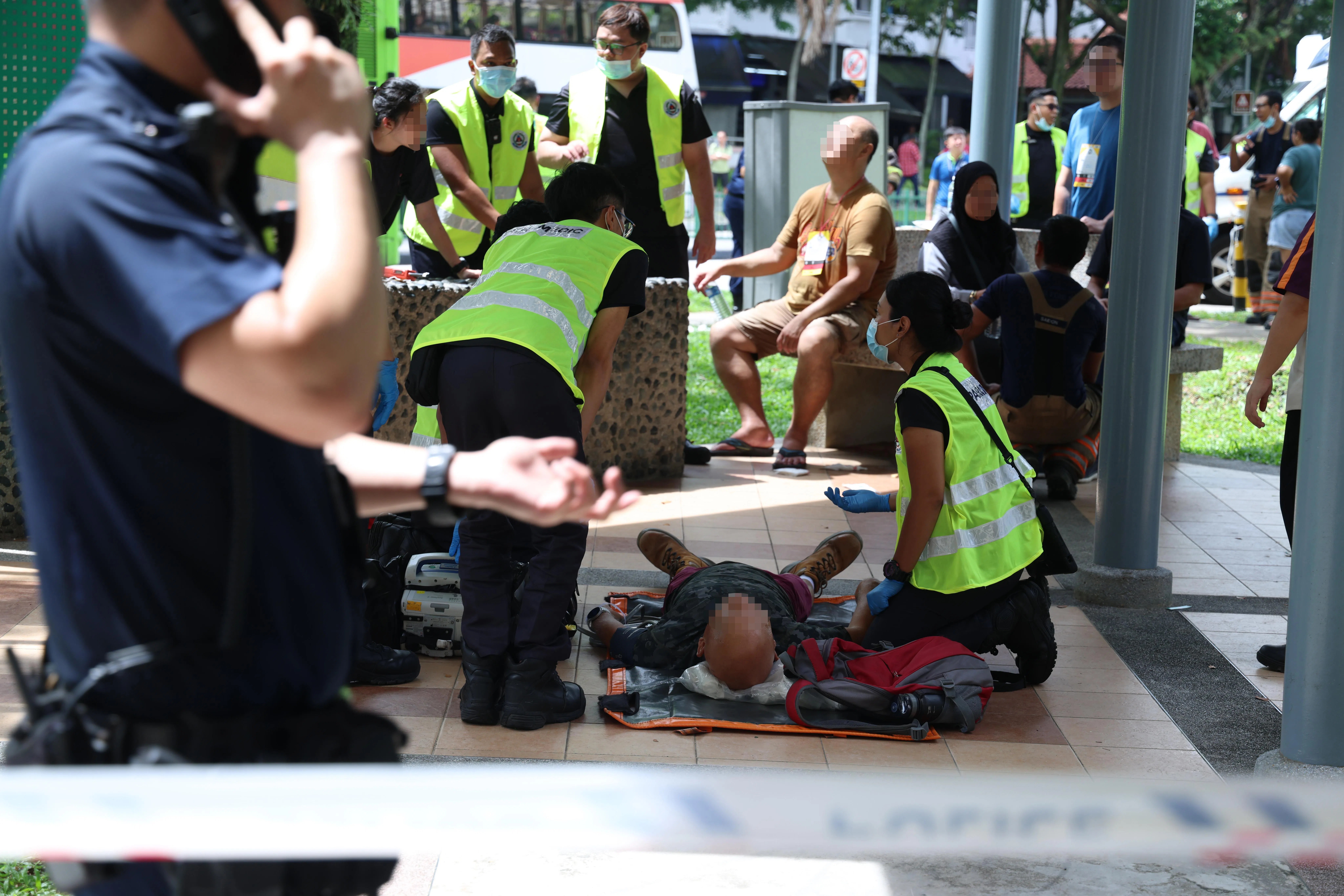 车祸发生后，多名伤者在封锁区内接受救护人员的检查和治疗，有的平躺在地上，有的坐石椅上或站着。（郑一鸣摄）
