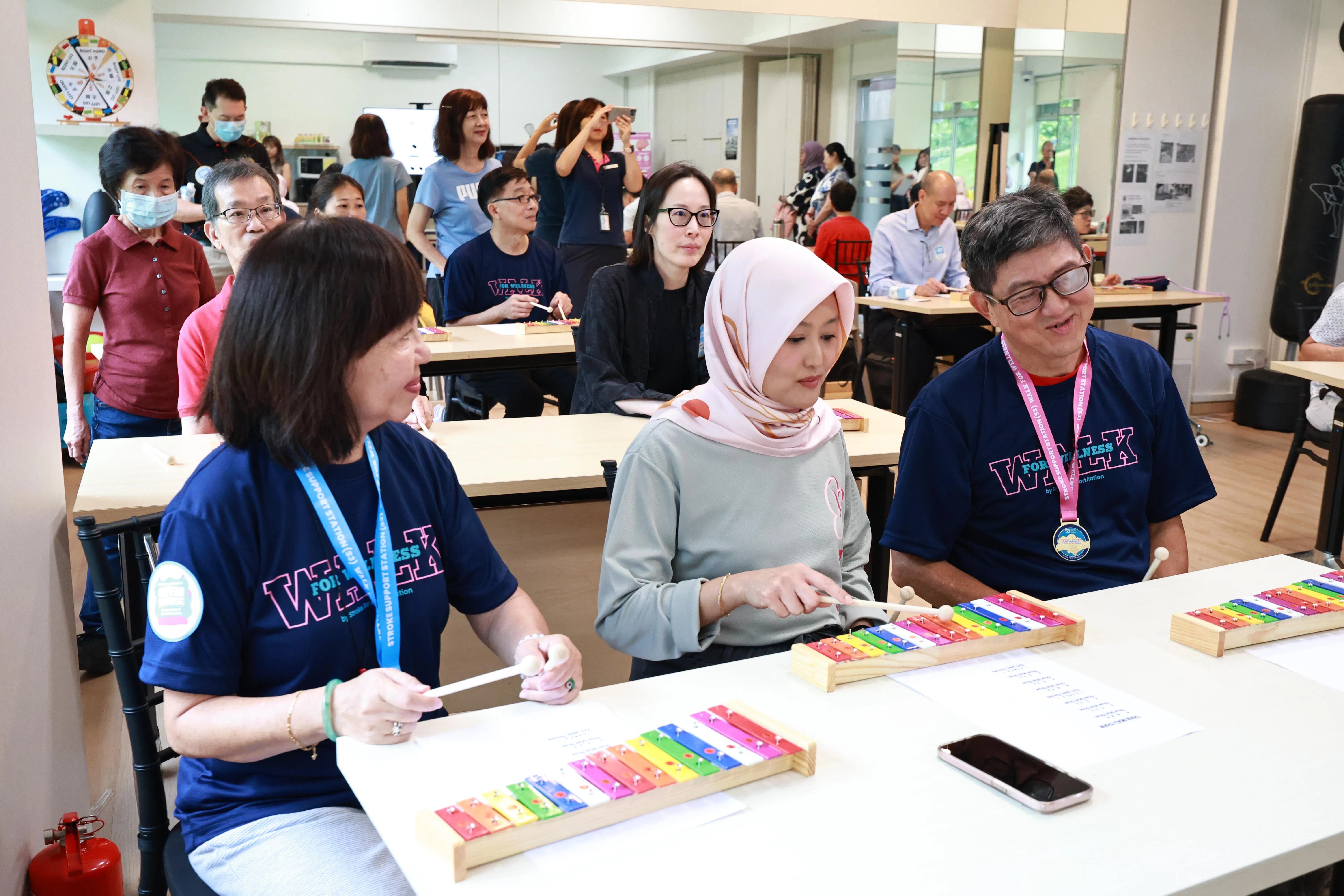 数码发展及新闻部兼卫生部政务部长拉哈尤（中）在中风援助中心开放日活动上，与患者等一同体验钟琴（glockenspiel）项目。（特约陈来福摄）