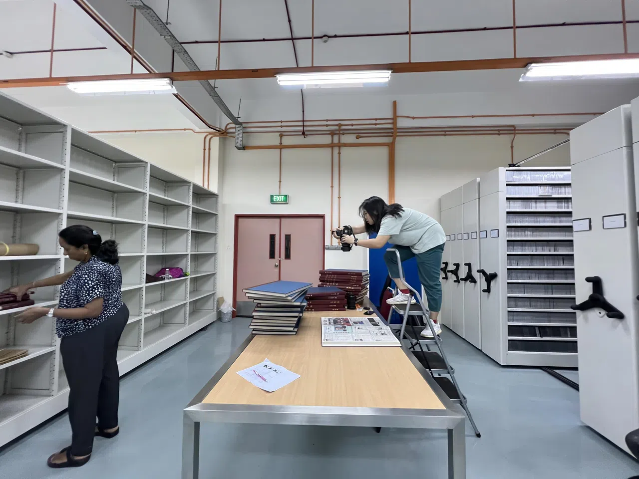 华文媒体集团将《联合早报》早年每一天的报纸按年份装订成册，收藏在内部资料室里。图为《我们》项目的摄影协调、早报摄影记者白艳琳翻拍早报的报章版面。（郭颖轩摄）