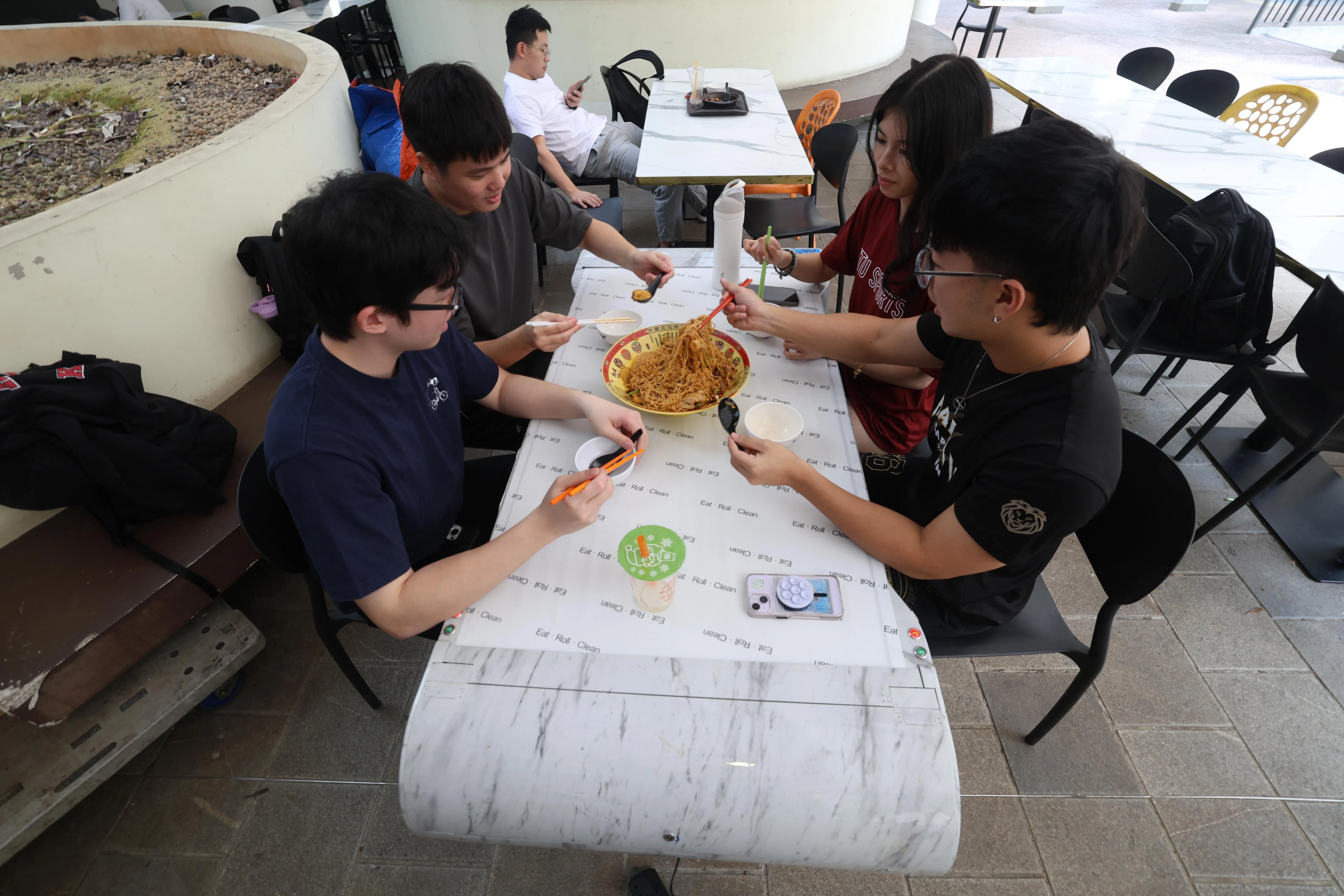 南大学生苏萨诺（左起）、陈杰康、温爱丽雅和陈伯旭，1月12日中午在听了工作人员介绍后，第一次在Pioneer Hall食阁的自动清洁桌用餐。（关俊威摄）