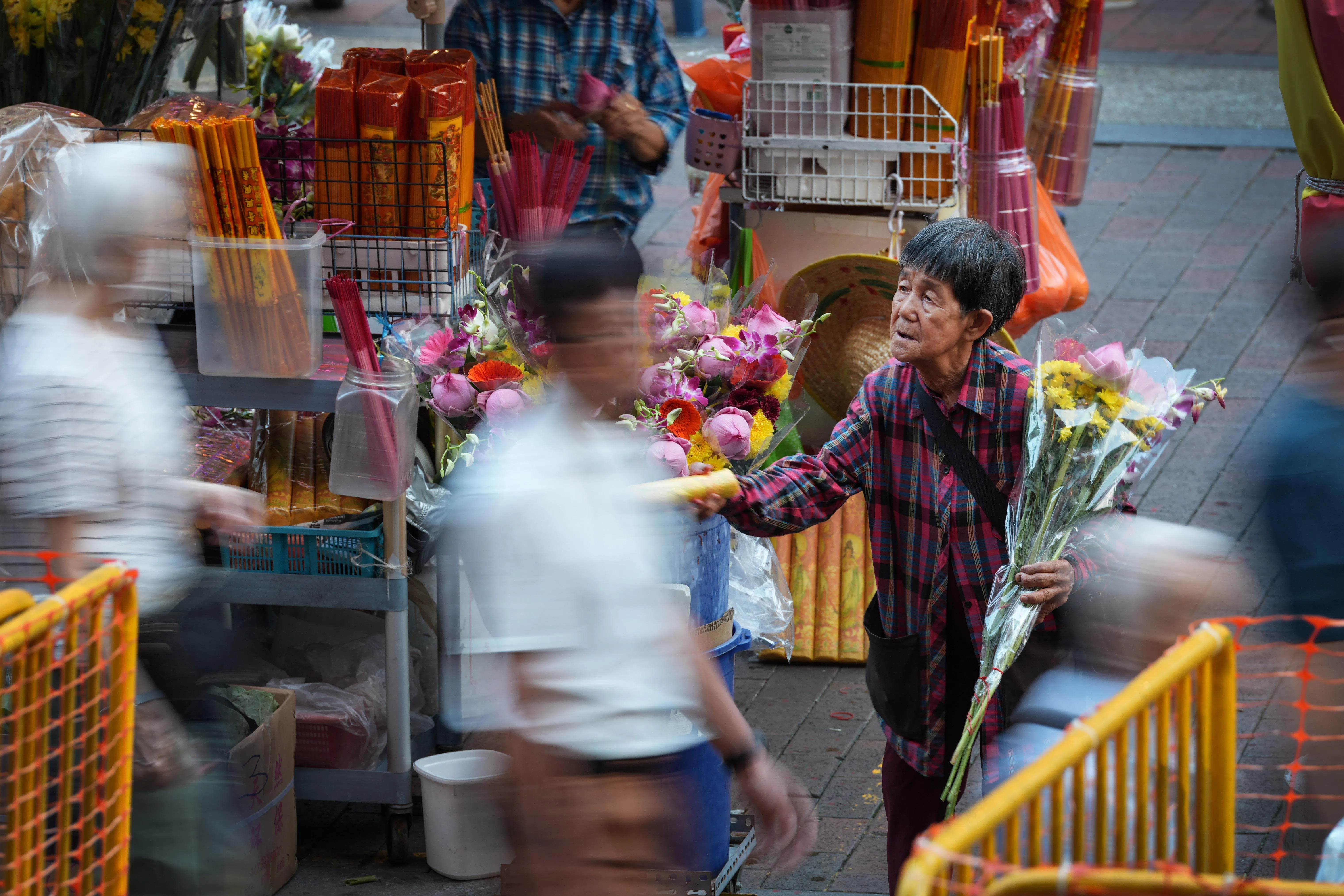 晨光熹微，数百名信徒中，一名头发灰白的阿婆格外安静，她手执鲜花，神情安然地向路过的信徒轻声探问。那一刻，虔诚与生计，都在她手中的花里。（何家俊摄）
