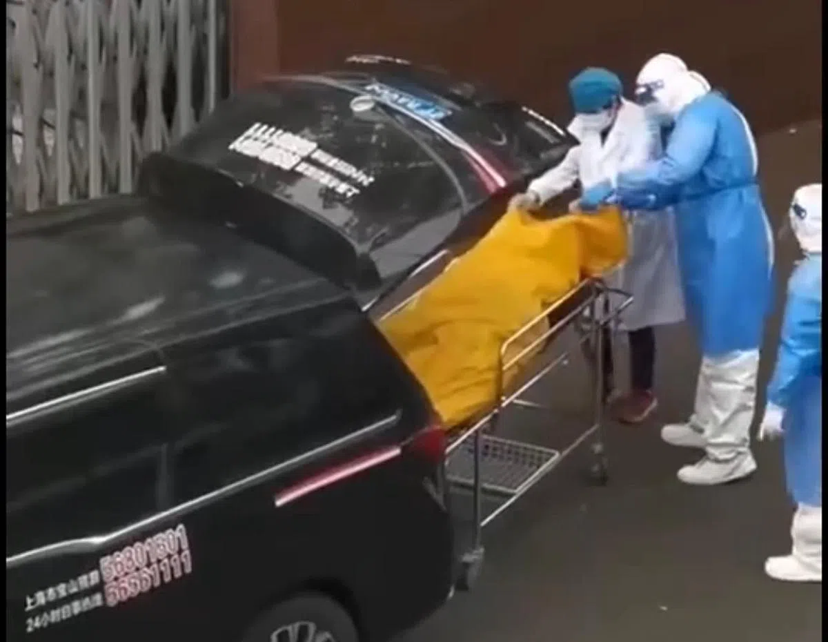 新长征福利院人员（左一）拉开袋子查看后，一度又将尸袋内的白布盖上，殡仪馆人员（蓝色防护衣者）见狀立即阻止，院方才将老人连同担架推回福利院。 （互联网）