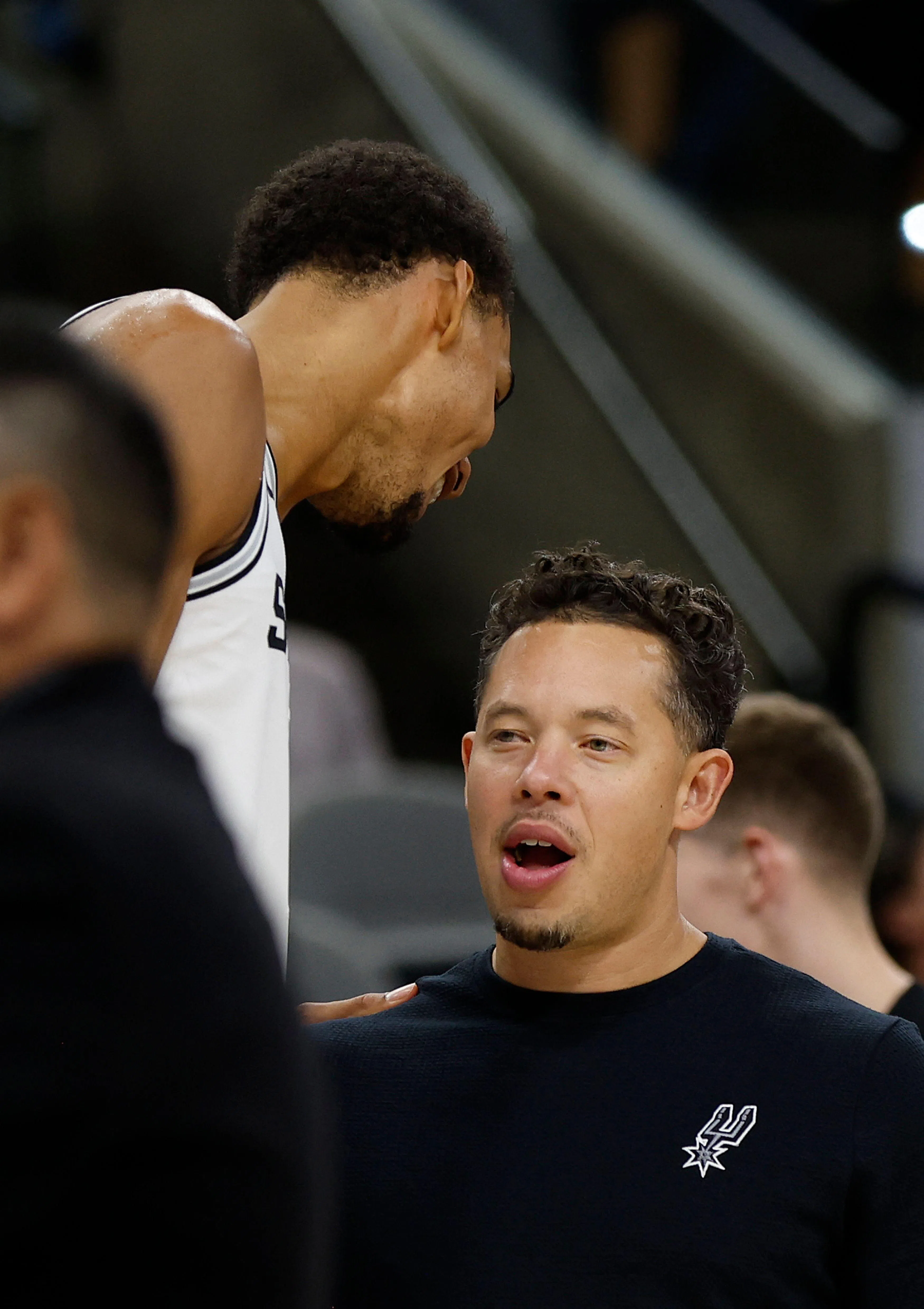 马刺新帅米奇·约翰逊（右）在赛中与文班亚马（左）交流。约翰逊在今年5月接过功勋主帅波波维奇的教鞭，后者在去年因中风入院，并在今年因身体等方面的原因转入幕后，担任球队篮球运营总裁。（法新社）