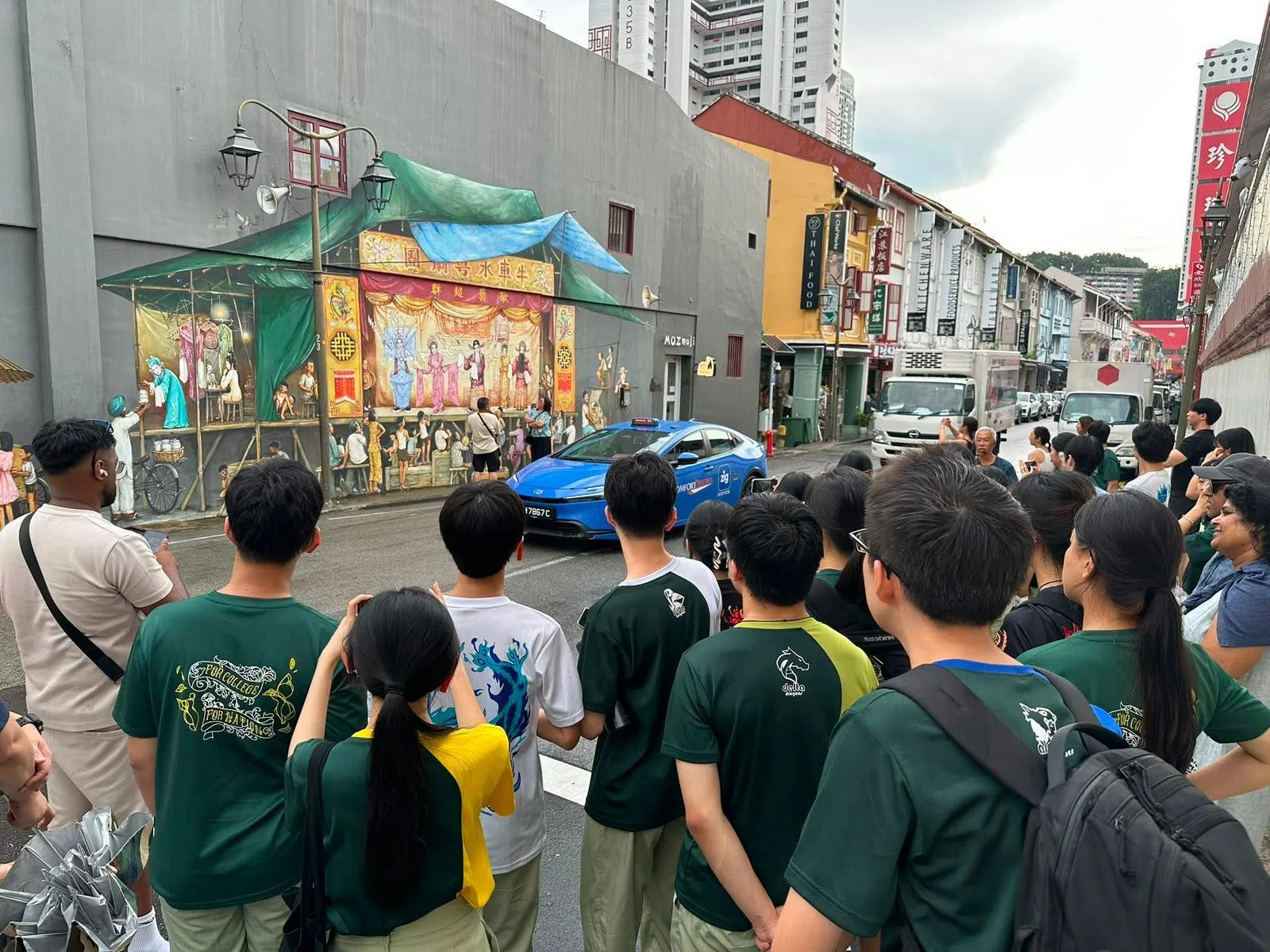 淡初语特生围在牛车水壁画前，用镜头捕捉社区历史。（新文潮出版社提供）