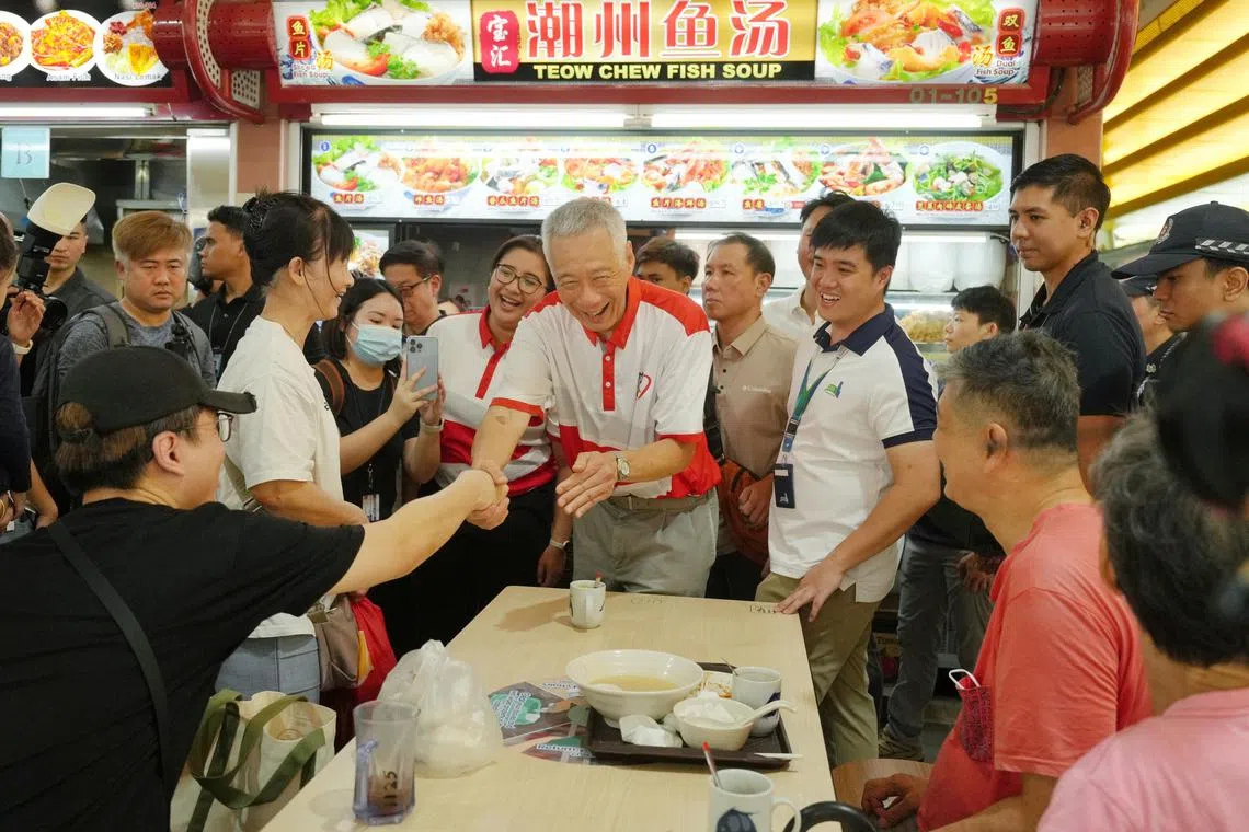 国务资政李显龙（中）与同为宏茂桥集选区议员的娜蒂雅（后方，身穿红白上衣）走访静山巴刹与小贩中心，一路受到居民的热烈欢迎。（谢智扬摄）
