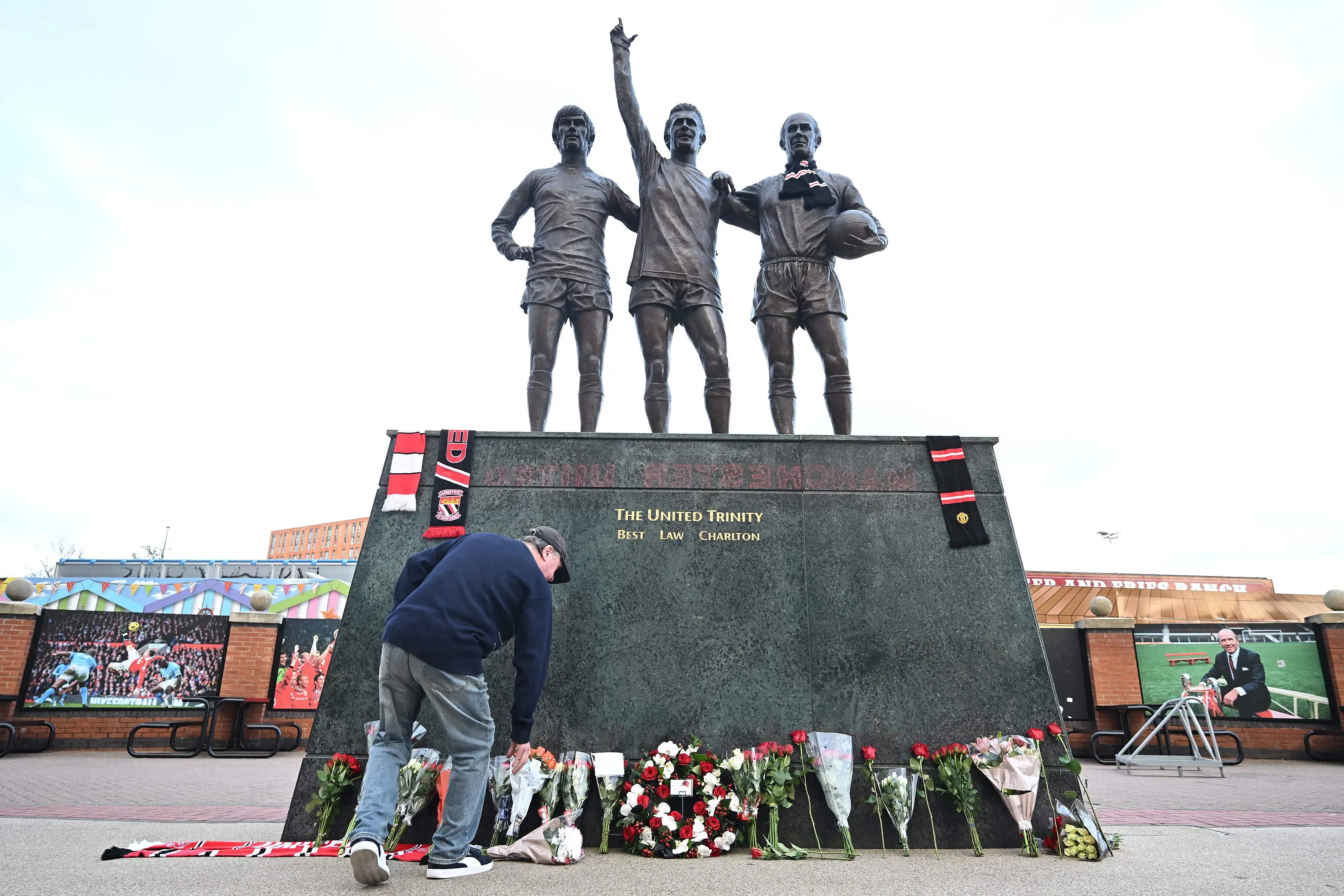人们在老特拉福德球场外的“红魔三圣”雕像面前献上祭品和鲜花，悼念查尔顿的离世。雕像三名球员分别是前曼联球员乔治·贝斯特（左起）、丹尼斯·劳和鲍比·查尔顿。（法新社）