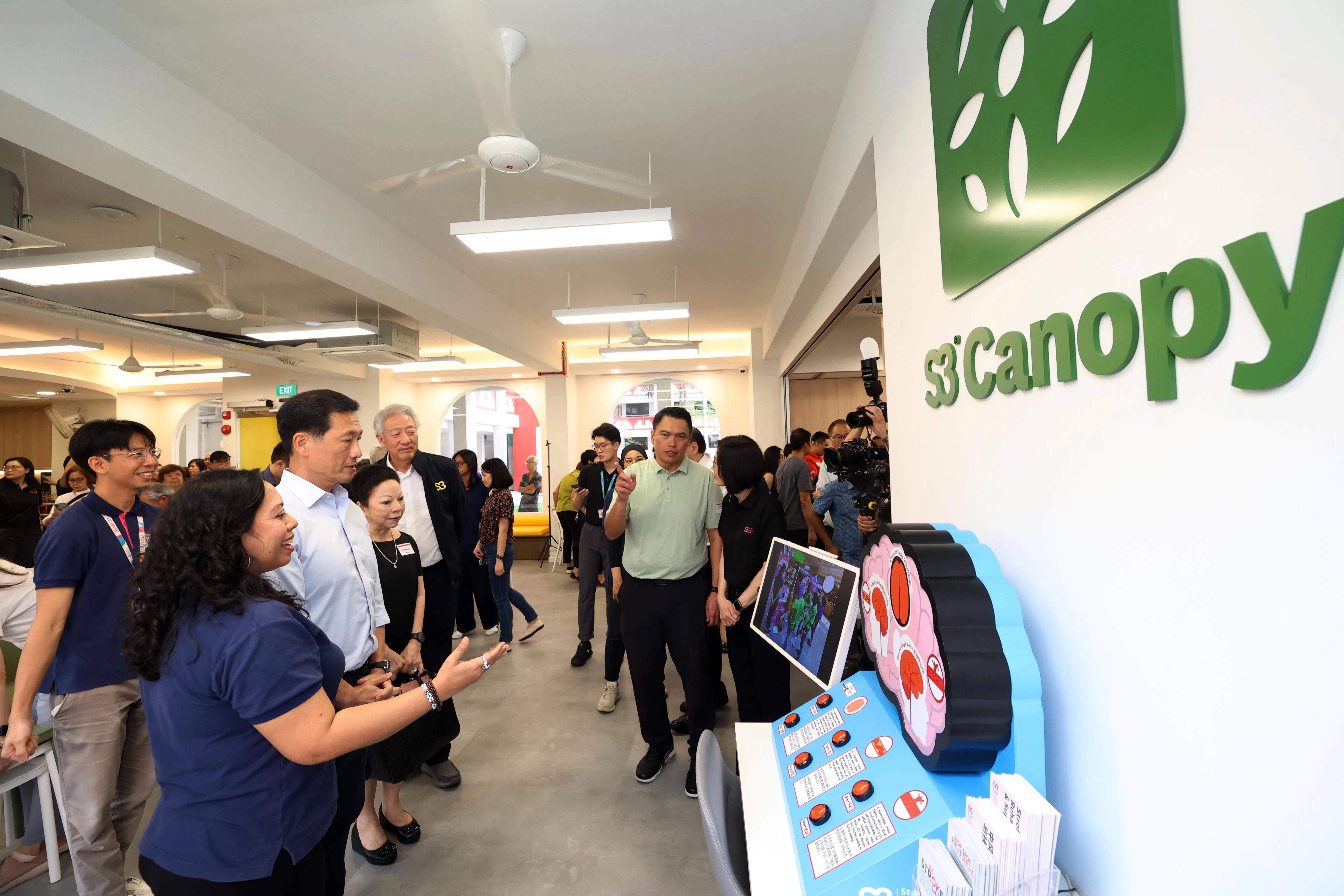 社会政策统筹兼保健卫生部长王乙康（左二）、总理公署高级顾问张志贤（左四，穿黑外套）和先驱区议员郑德源（右二，穿绿色上衣），一同参观S3康乐陪活跃乐龄中心里的“大脑机器”。这套器材会生动讲解不同类型中风是如何形成的。张志贤也是S3赞助人。（邝启聪摄）