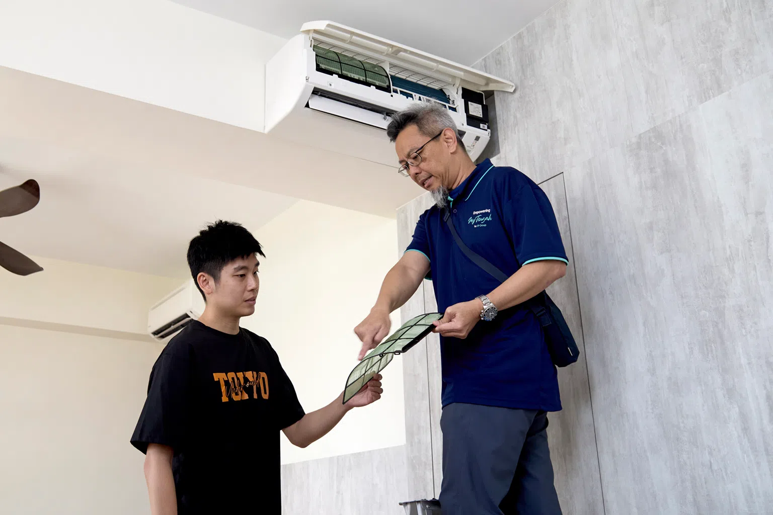 新能源集团的技术人员在一次保修服务中向黄子洋（左）解释常见的冷气系统问题。（新报业媒体）