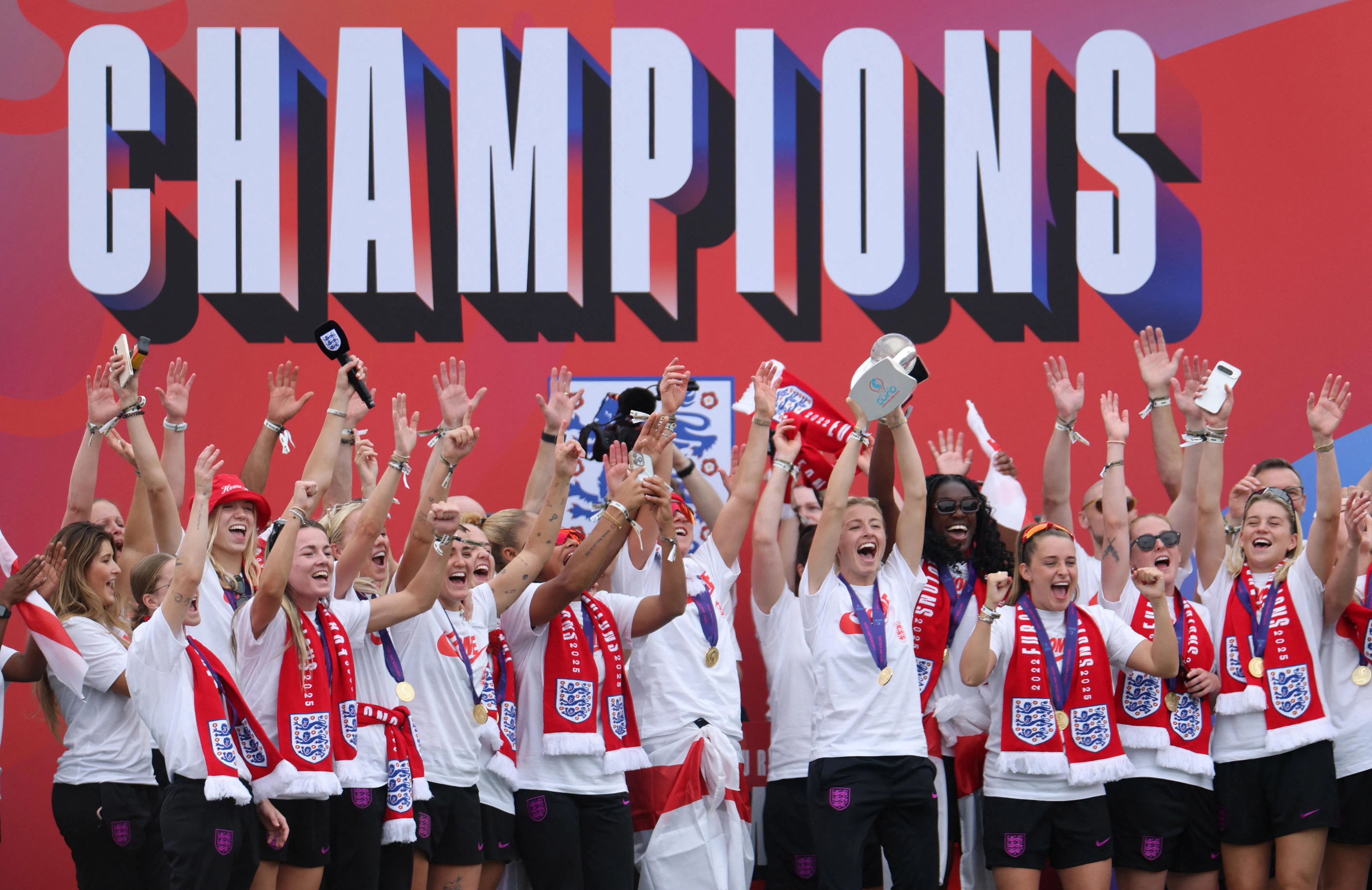 庆祝游行在白金汉宫前的舞台结束，英格兰女足队长利亚·威廉森（举杯者）高举奖杯与众人分享喜悦。（路透社）