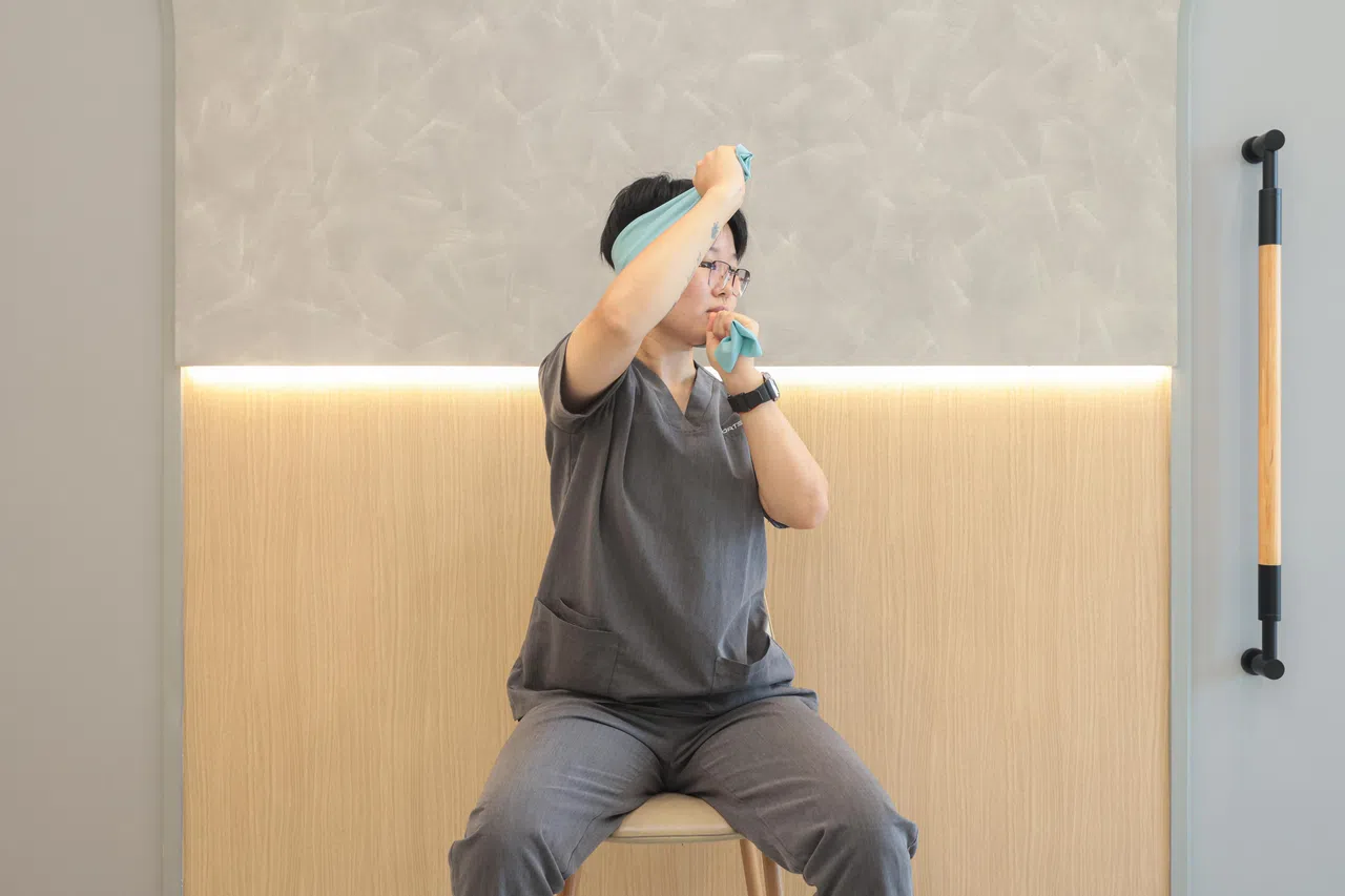 左手弹力带紧靠耳朵下方，右手弹力带紧靠耳朵上方。右手向左用力，让毛巾带动头部向左旋转至最大角度。（李冠卫摄）