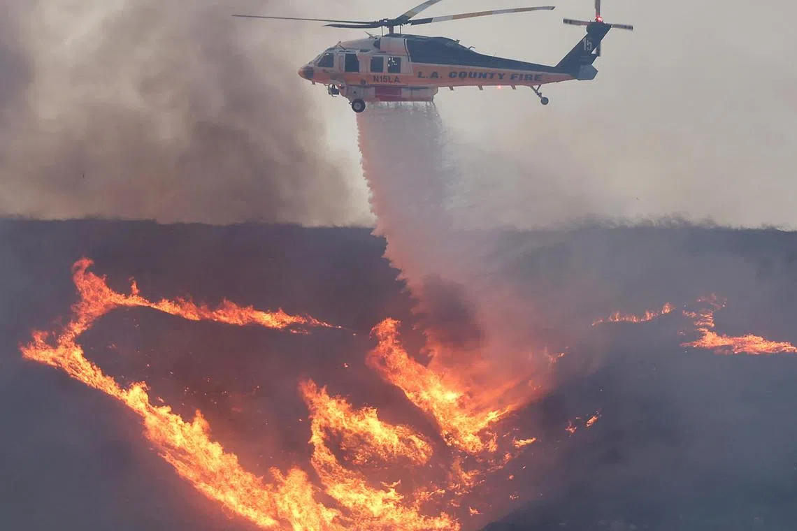 南加州洛杉矶县西北部卡斯泰克湖附近燃起新的山火，图为一架消防直升机从空中洒水救火。（法新社）