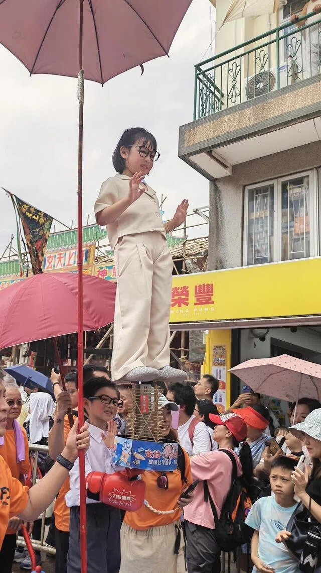 约20台飘色车轮流巡游，这台以“大楼围标”为主题，上方小妹妹扮演女性政府官员，底下小弟弟扮演保安局局长邓炳强。（陈爱薇摄）
