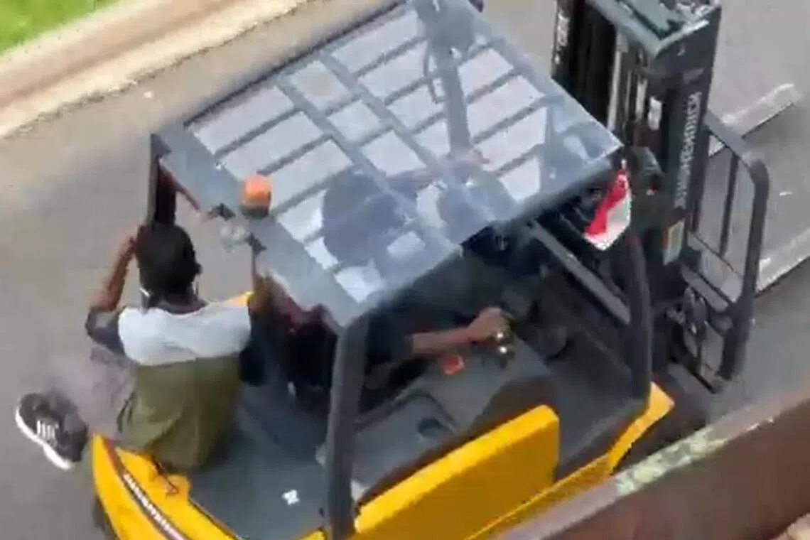 叉车完成作业后驶离垃圾箱时，有个工人跳上叉车搭顺风车。（视频截图）