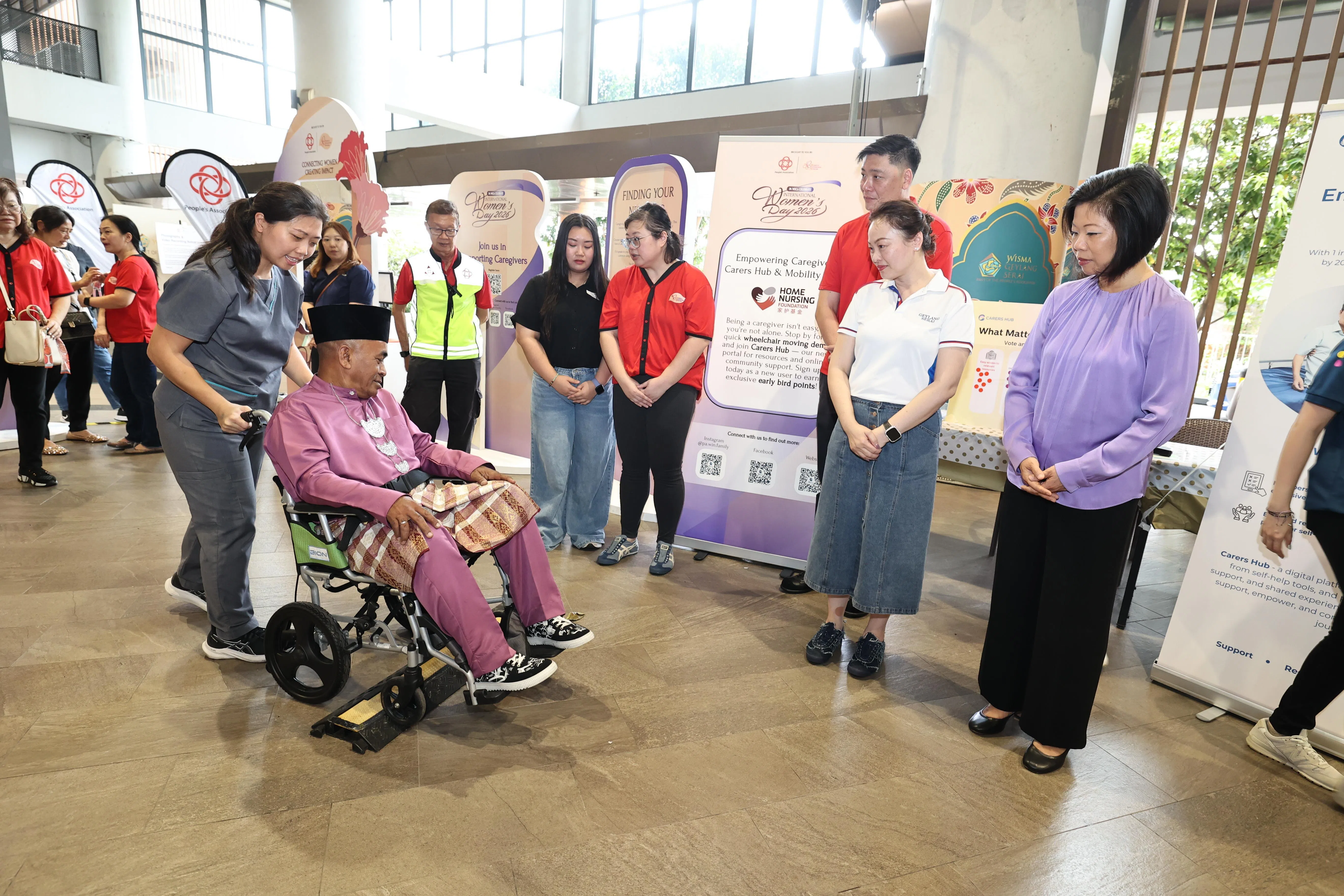 沈颖（右一）观摩了家护基金（Home Nursing Foundation）员工示范如何安全使用轮椅通过路面障碍。参与示范的是65岁的志愿者穆罕默德·再拉尼（Mohamed Zailani）。（周国威摄）