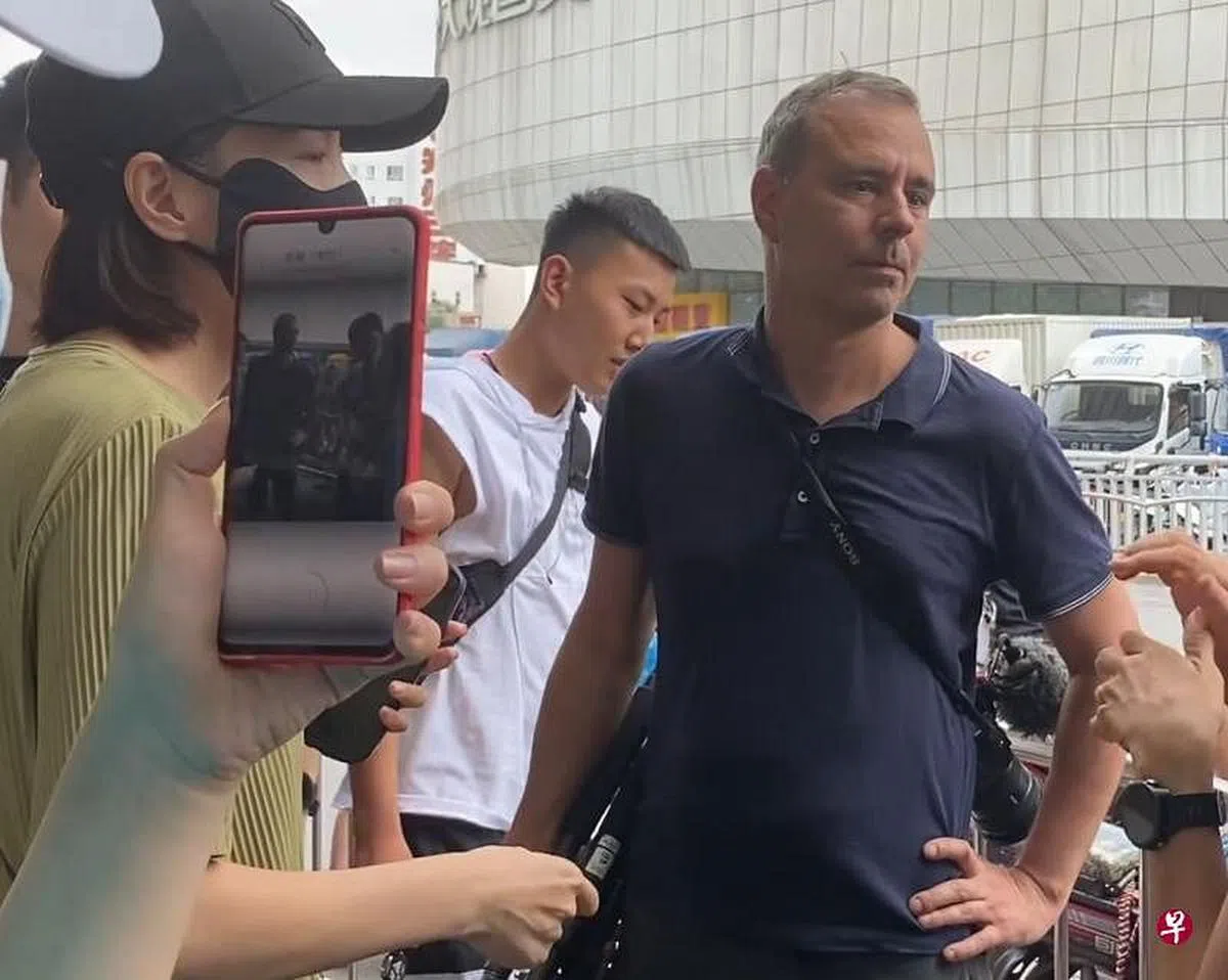 微博网民发出的视频显示，德国之声记者伯林格（Mathias Boelinger，右）7月24日在郑州被民众包围，一名戴黑口罩的女子（左二）劝请民众冷静。（“vanessa言午”微博账号视频截图） 