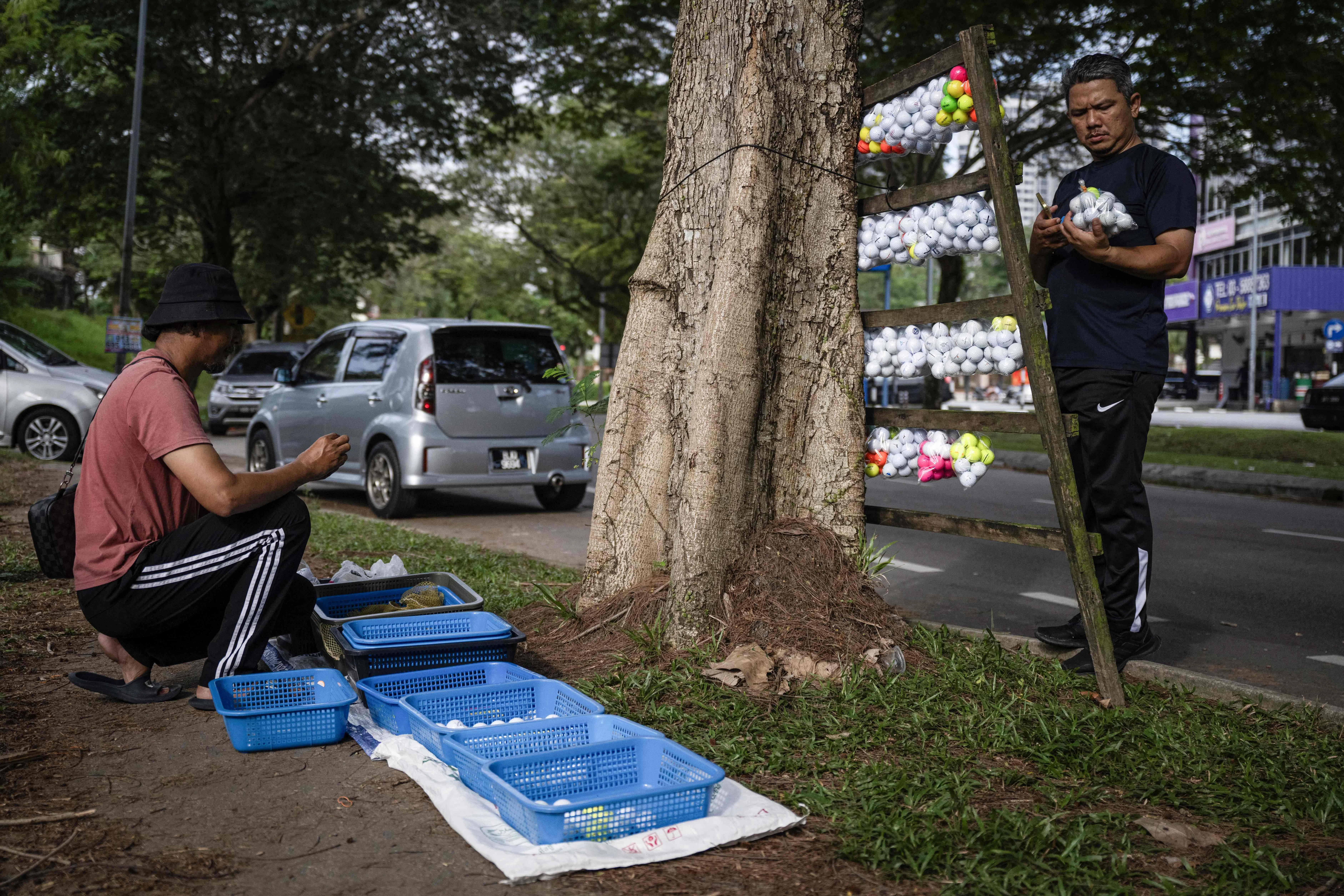 苏马迪（左）每周工作三天，每次能找到500至600颗球，每逢星期六上午在一家高尔夫球场入口处摆个简陋摊位，以每份20颗球出售他的战利品。（法新社）