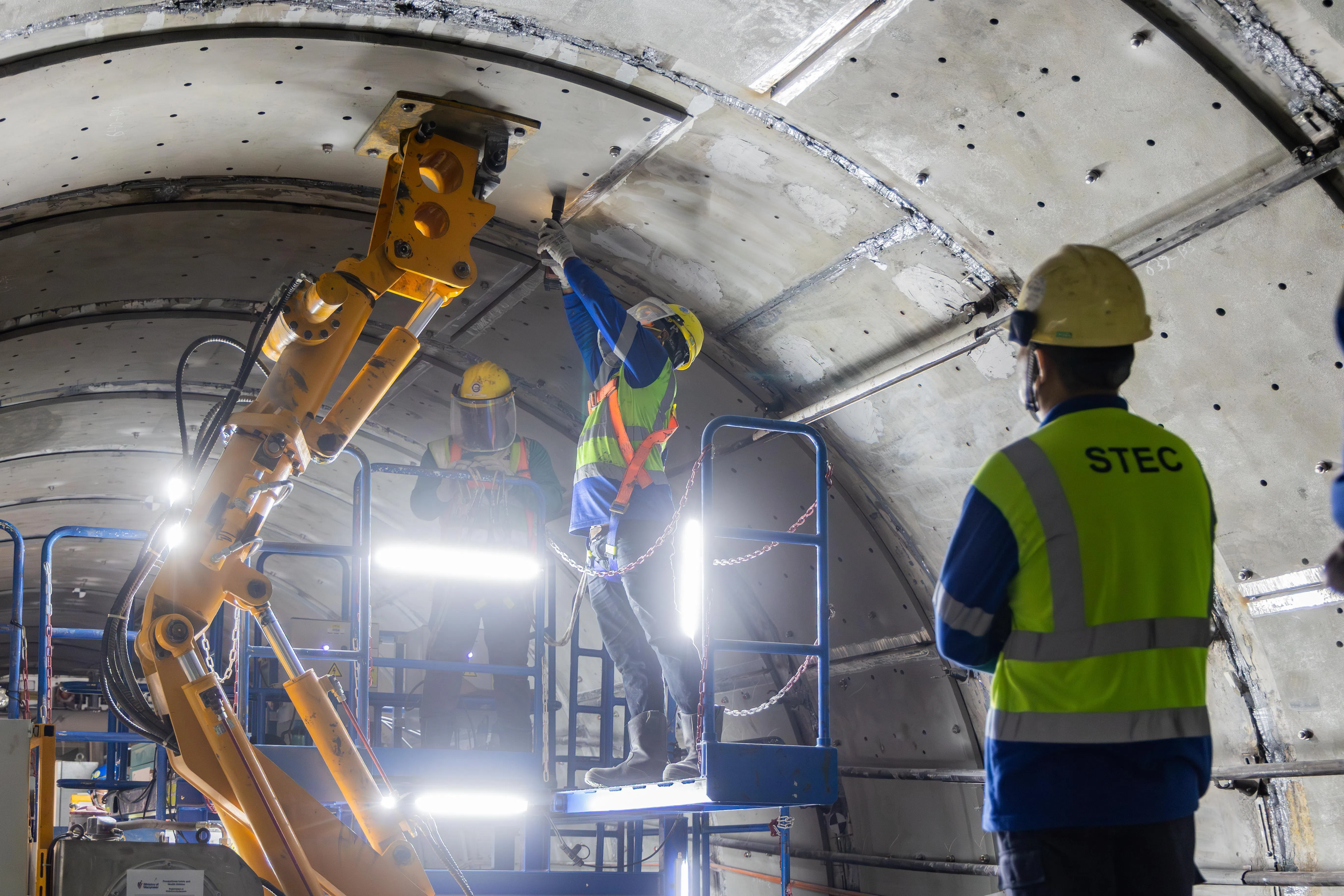 在机械臂的辅助下，一名操作员“举起”量身定制的钢板，准确移动到要固定的位置后，再由另两名员工拴牢。（吴先邦摄）