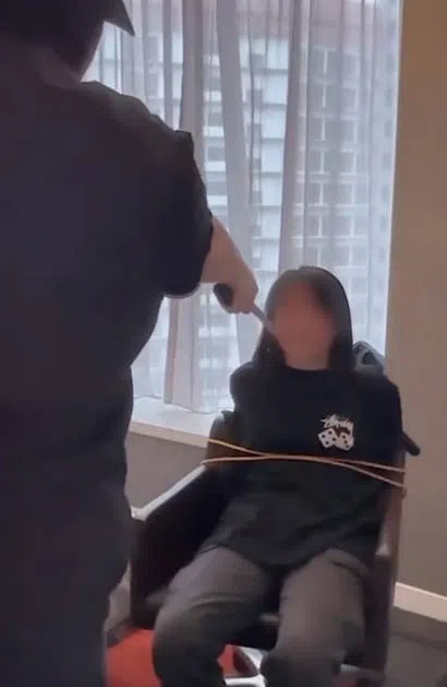 被捕的25岁男子拿着一把反曲刀（Kukri knife）指着被捆绑囚禁在椅子上的女子，拍摄视频制造绑票假象。（新加坡警察部队提供）