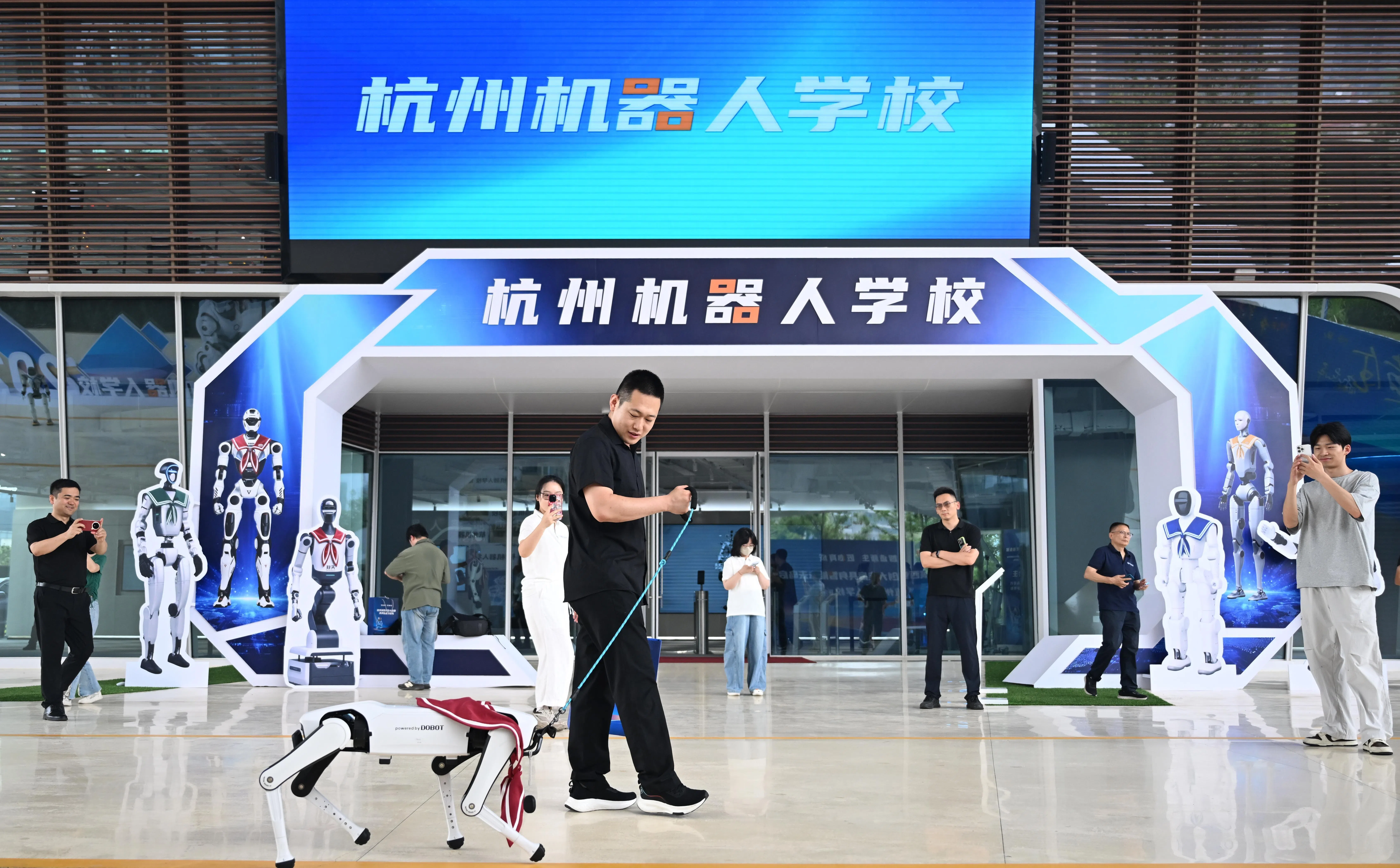 杭州机器人学校星期一（6月29日）揭牌，图为一名体验者在杭州机器人学校门口遛“机器狗”。（中新社）