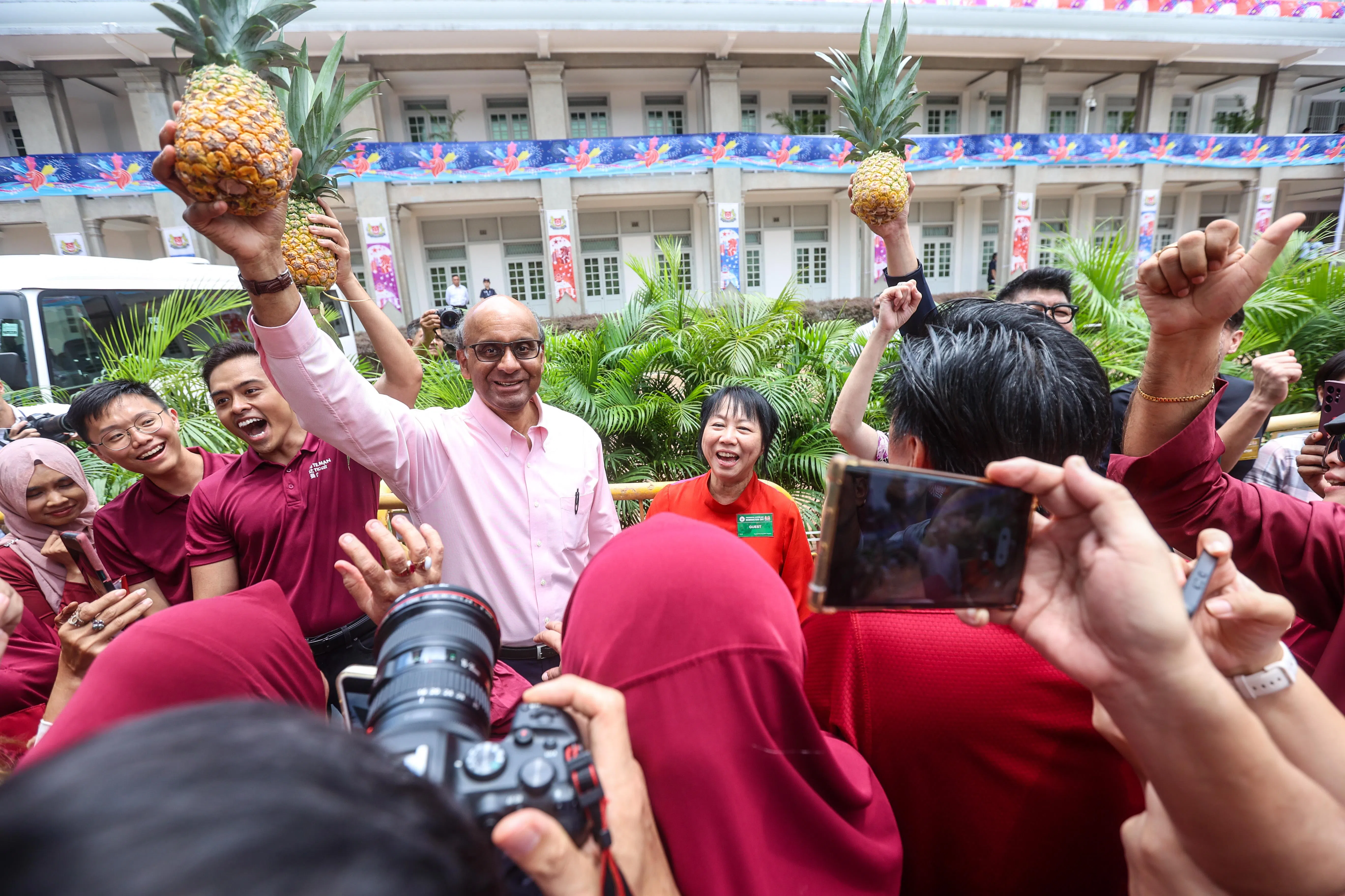 尚达曼（粉红上衣）选择黄梨为竞选标志，他在离开提名中心前高高举起支持者递给他的黄梨。在他左边的是夫人珍一藤木。（关俊威摄）