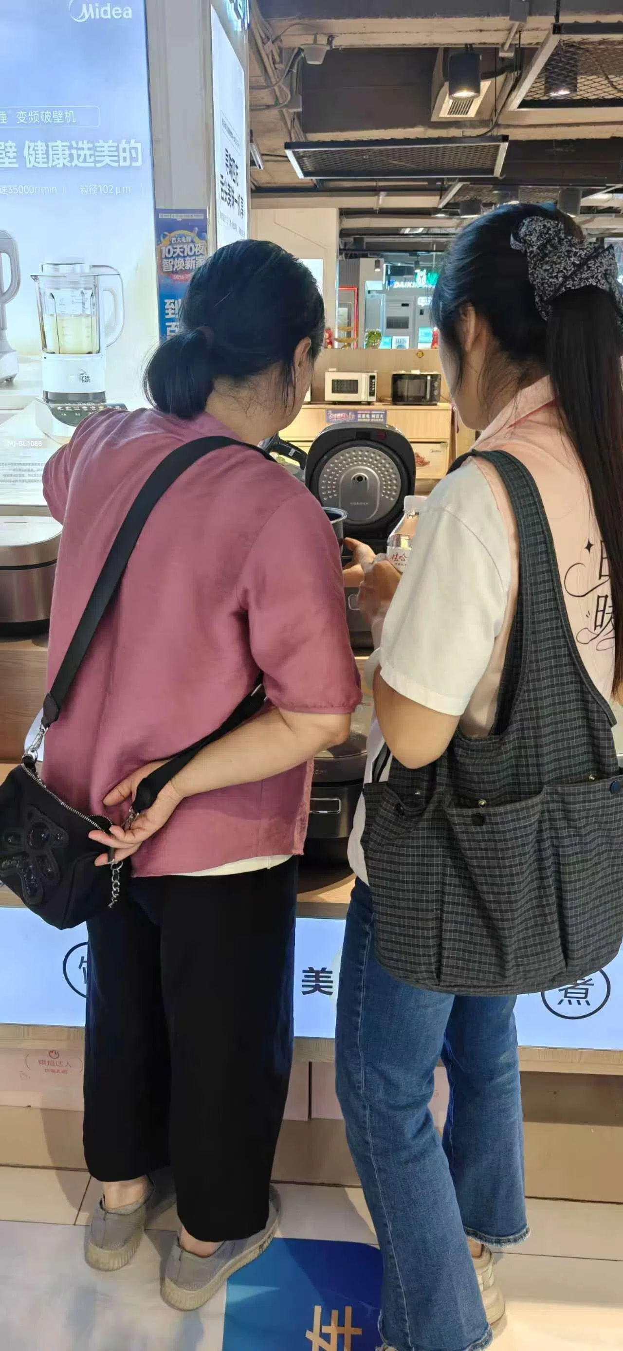 养老陪伴师陪老人家话家常，也帮忙跑腿、代办、陪诊、陪买家电等。图为“时光伴客”平台的陪伴师（右）陪同长者在商场挑选电饭煲。（受访者提供）